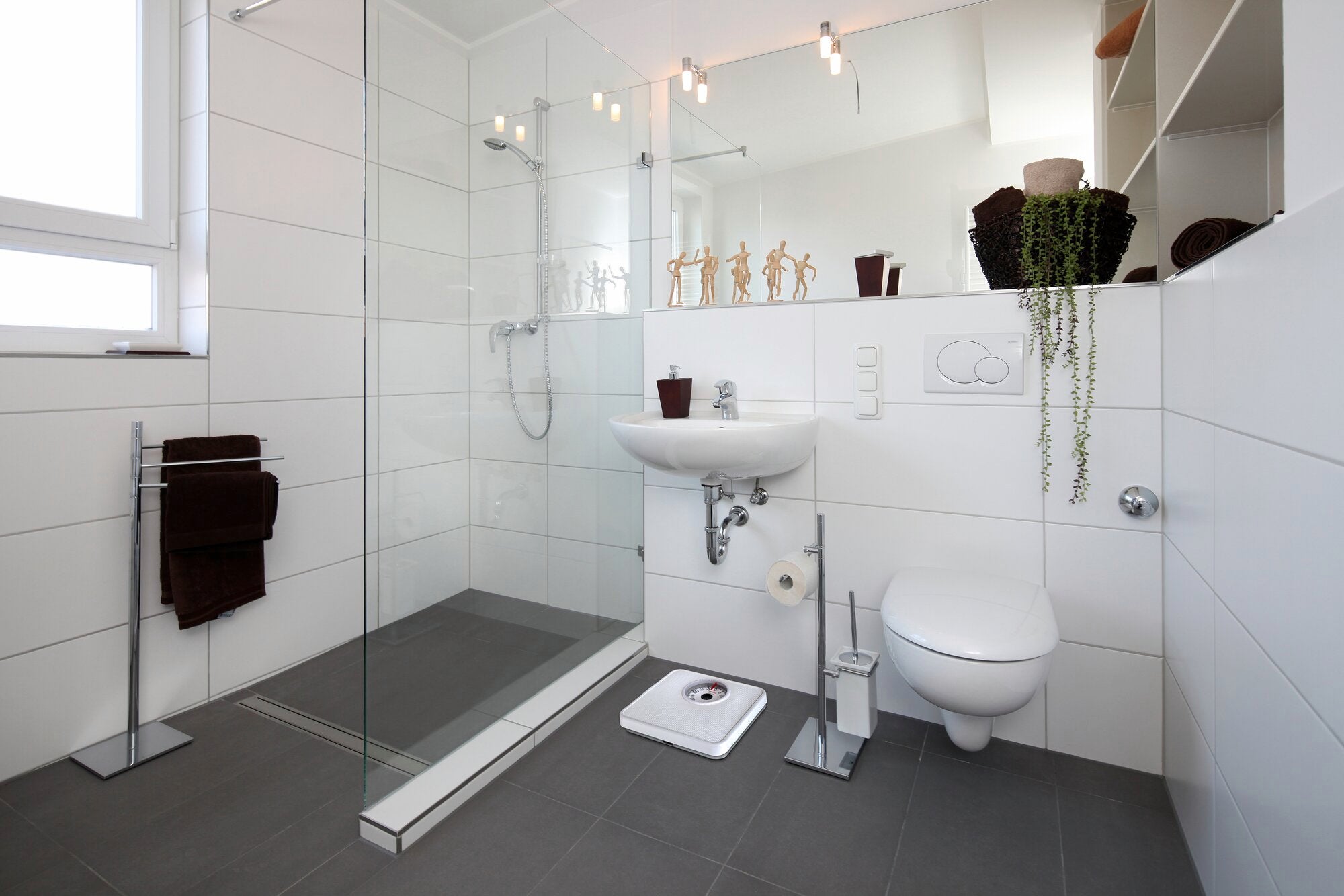 Digital bathroom scales in a modern bathroom with glass shower, sink and toilet. The scales are white and fit perfectly into the stylish, minimalist design of the room.