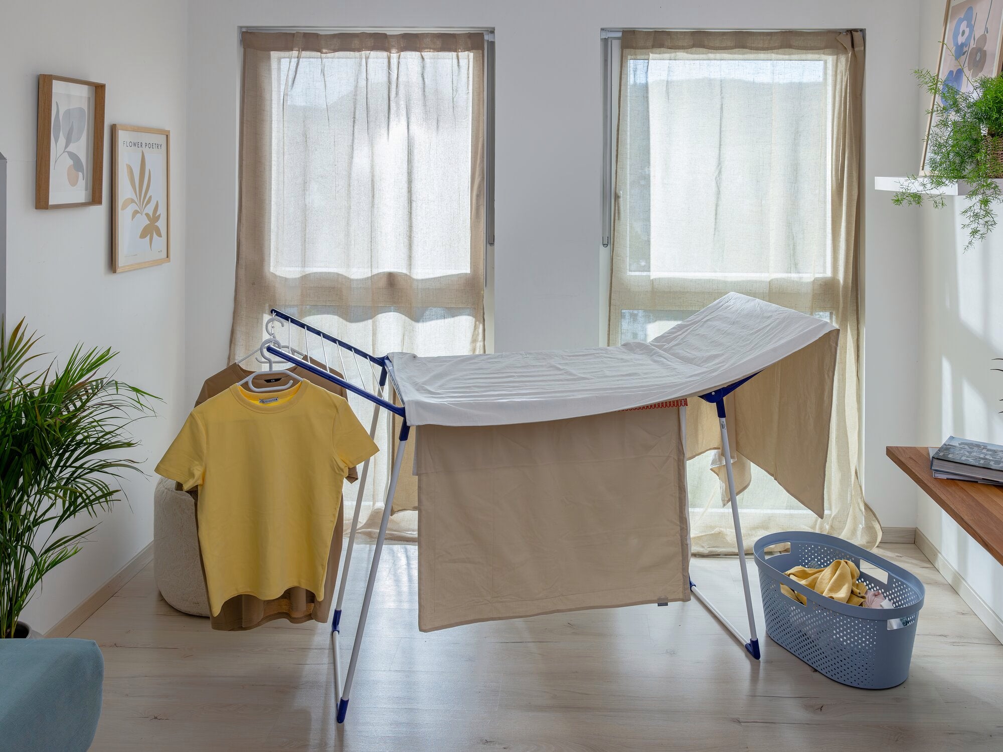 Pegasus 200 Solid Comfort wasdroger in een lichte kamer met twee ramen. De wasdroger is geladen met beige wasgoed, ernaast staat een mand met opgevouwen kleding. Ideaal voor efficiënt drogen.
