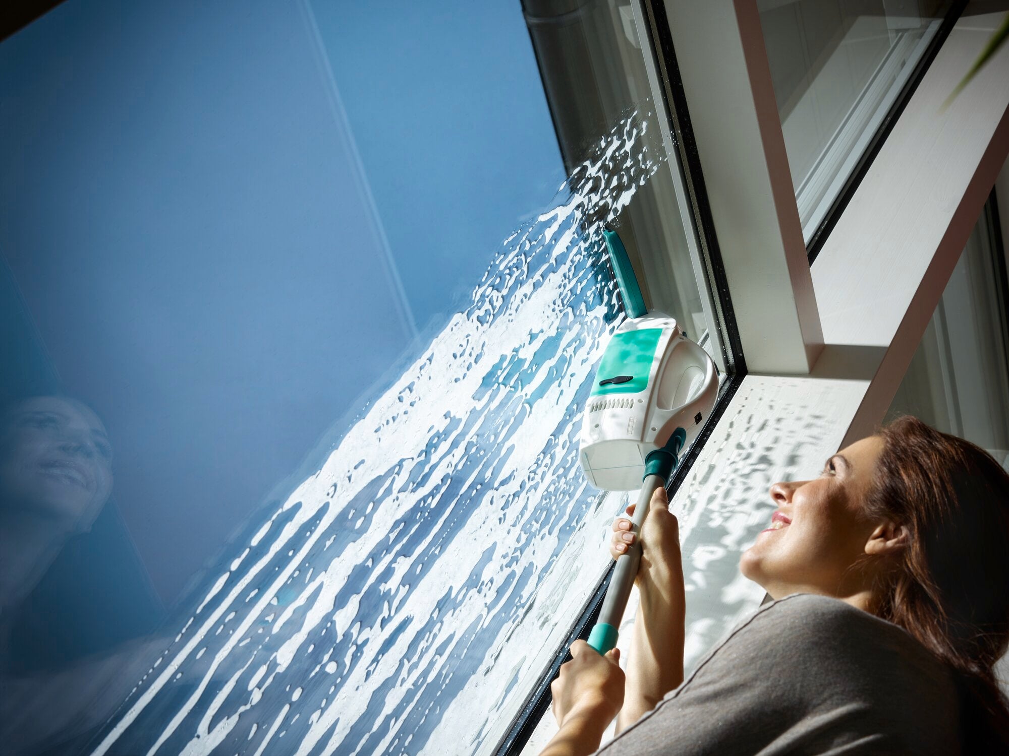 Eine Frau reinigt ein großes Fenster mit dem Fenstersauger Dry and Clean. Der Sauger entfernt effizient Wasser und Schmutz, während die Frau lächelt und die Sonne hereinscheint.