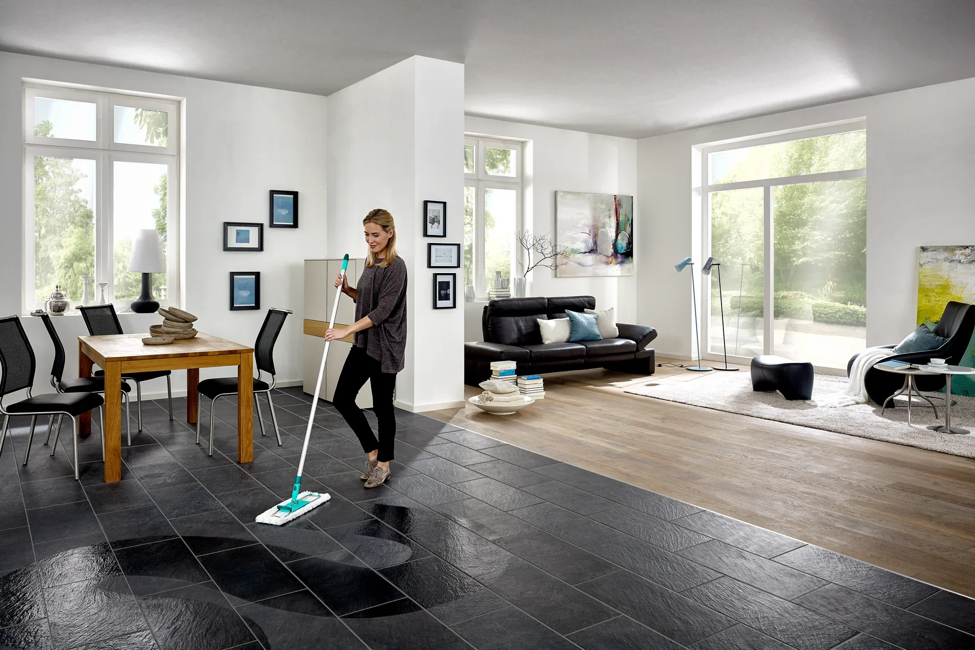 Een vrouw dweilt de vloer van een moderne woonkamer met de Profi XL dweilmop. De kamer is licht en stijlvol ingericht, met grote ramen en elegante meubels.