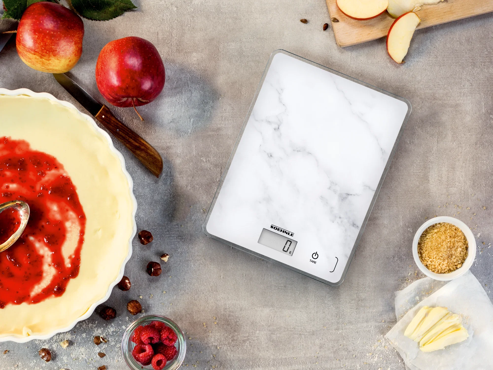 Page Compact 300 digital kitchen scales in marble look on a work surface. Surrounded by apples, raspberries, nuts and a bowl of red dough. Ideal for baking.
