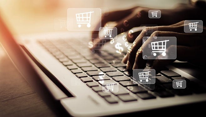 Haende tippen auf Laptop-Tastatur; darueber schwebende Einkaufssymbole und Dollarzeichen symbolisieren Online-Shopping.