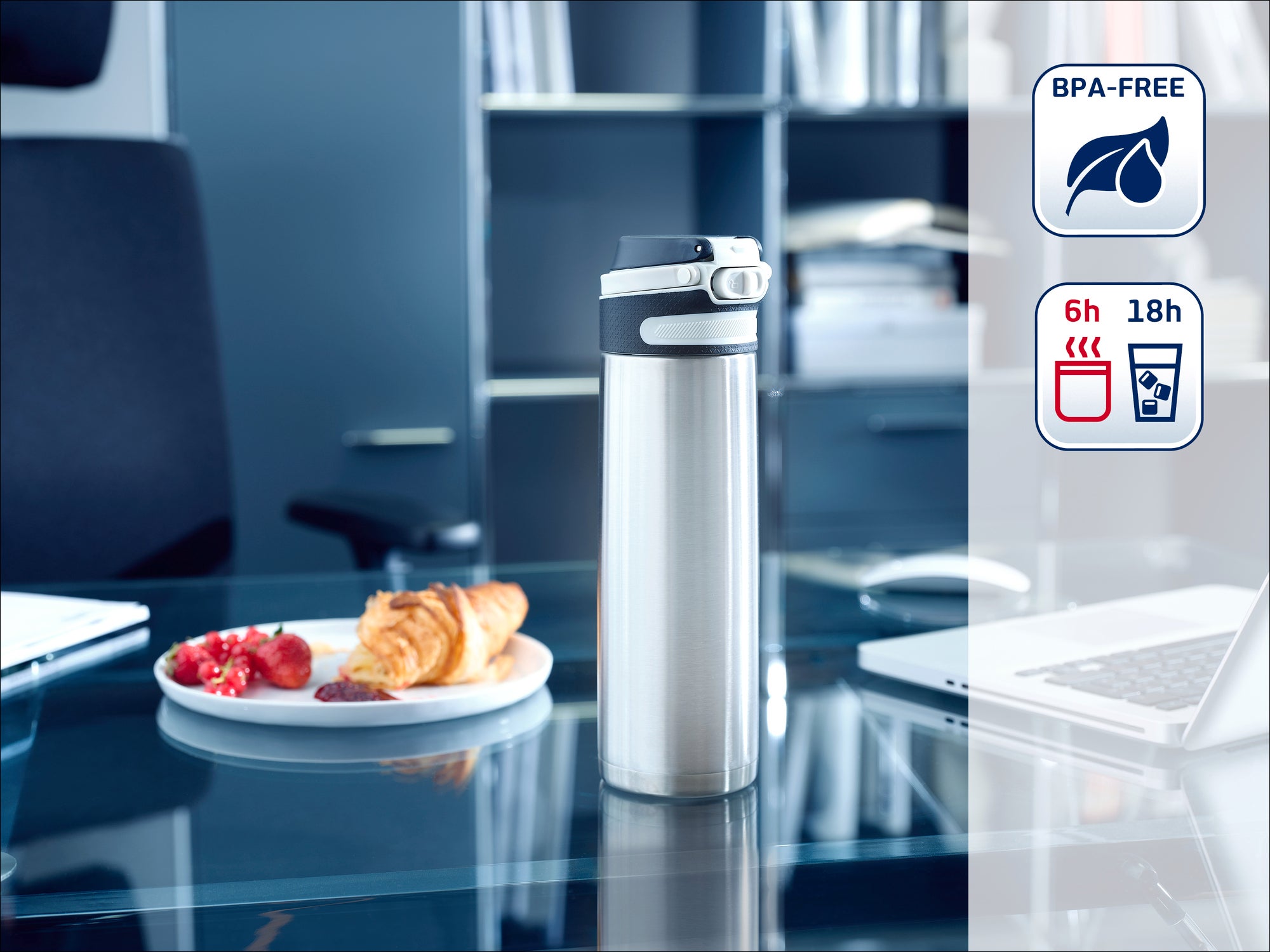 Une bouteille thermos en acier inoxydable est posée sur un bureau moderne à côté d'une assiette avec des biscuits. Des étagères sont visibles à l'arrière-plan. La bouteille est sans BPA et garde les boissons chaudes pendant 6 heures et froides pendant 18