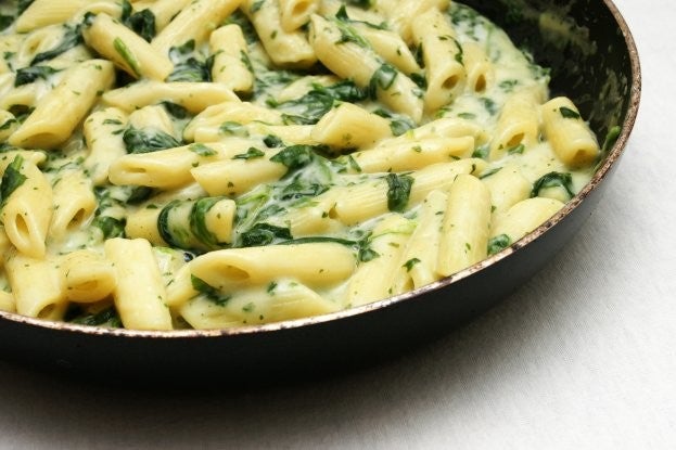 Cremige Spinat-Feta-Penne in einer Pfanne, serviert auf einem hellen Untergrund.