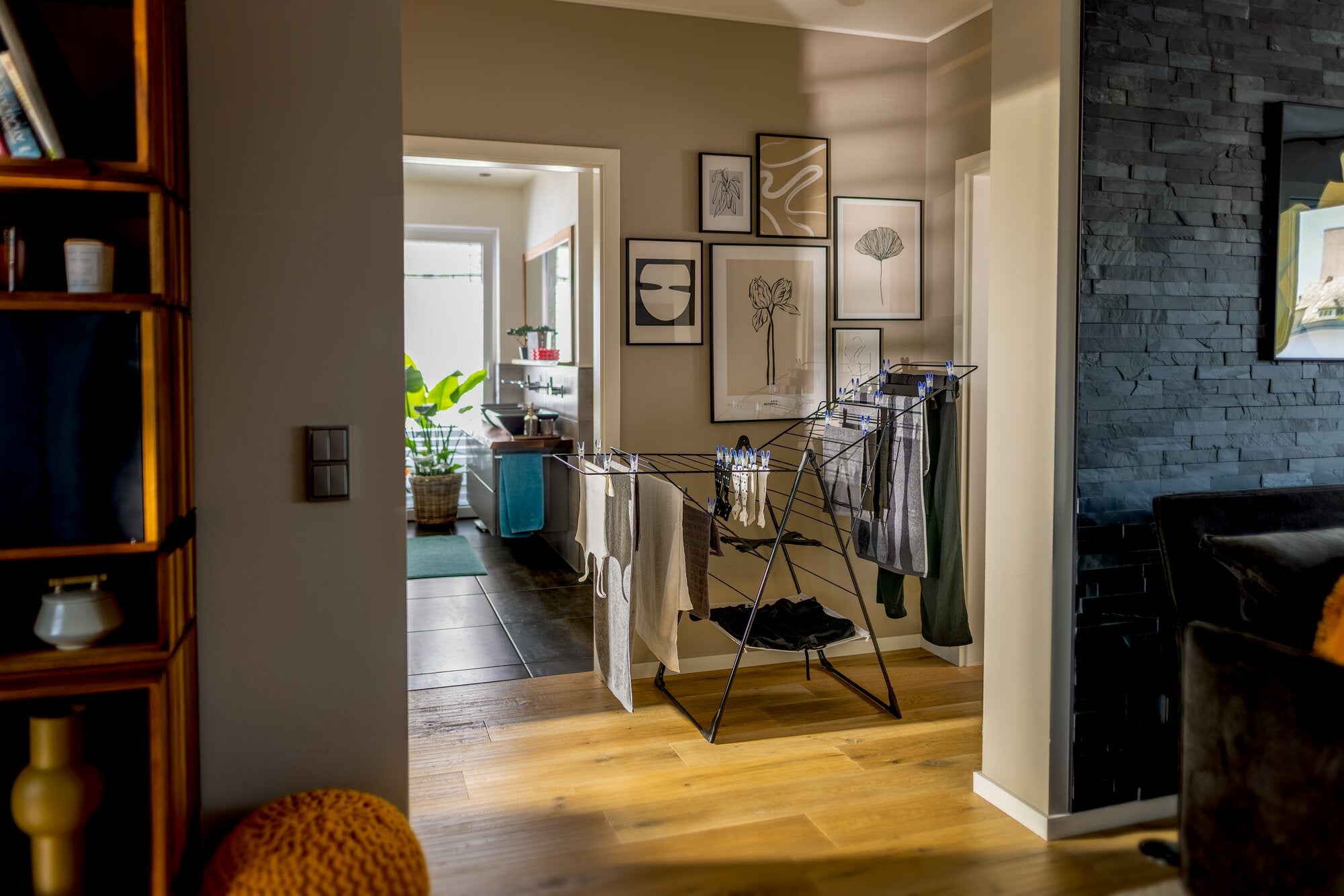 Leifheit Standtrockner Classic 250 Flex Black in modernem Wohnraum, mit mehreren aufgehängten Kleidungsstücken auf schwarzem Gestell; platzsparend auf Holzfußboden nahe dem Flur positioniert.