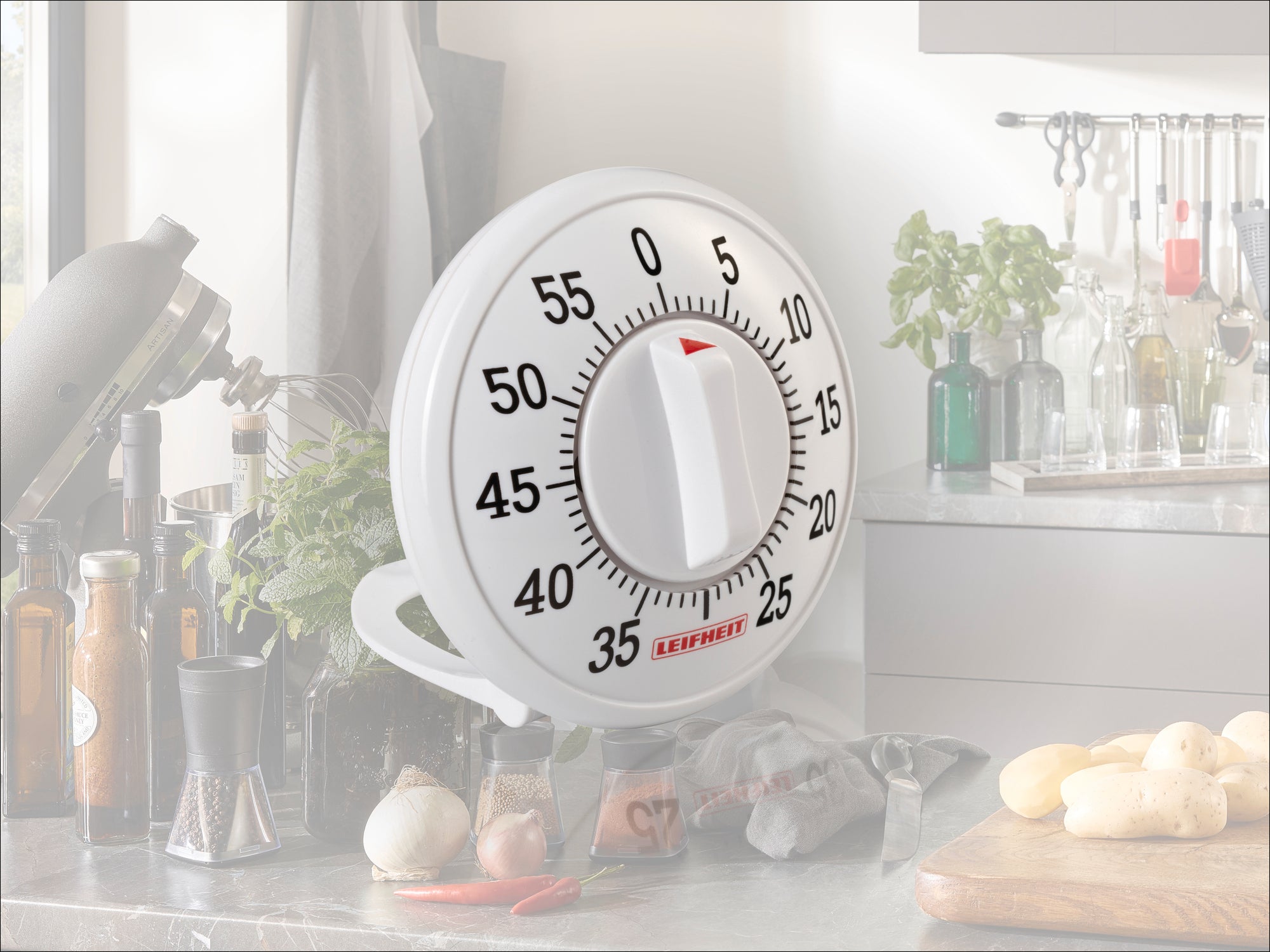 Ein weißer Küchen-Timer von Leifheit mit großer, gut lesbarer Skala von 0 bis 60 Minuten. Der Timer steht auf einer Küchenarbeitsplatte, umgeben von Kräutern und Gewürzen.