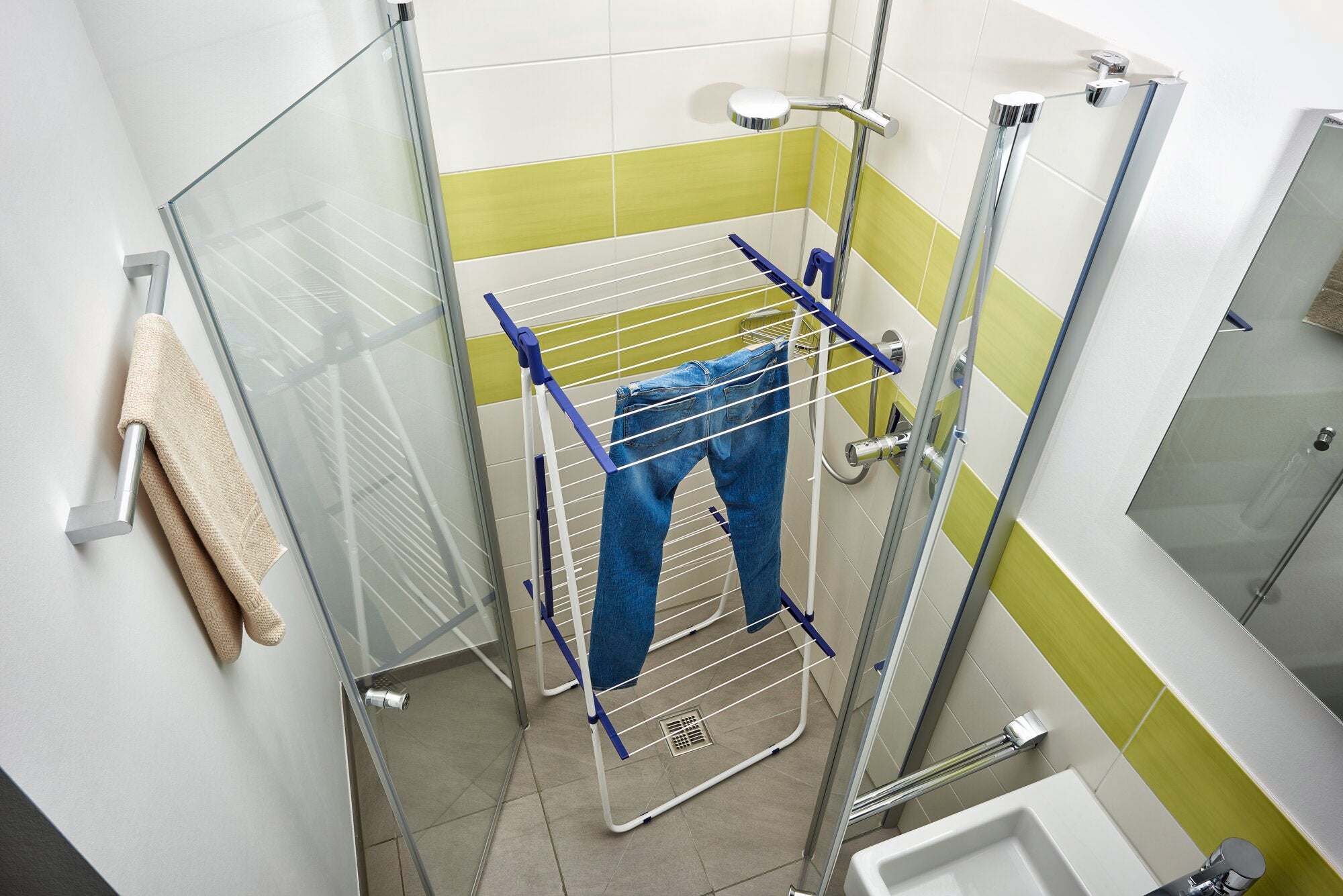 Un séchoir à linge Pegasus Tower 190 se trouve dans une douche moderne et lumineuse. Il est équipé d'un jean bleu et offre une solution peu encombrante pour sécher les vêtements.