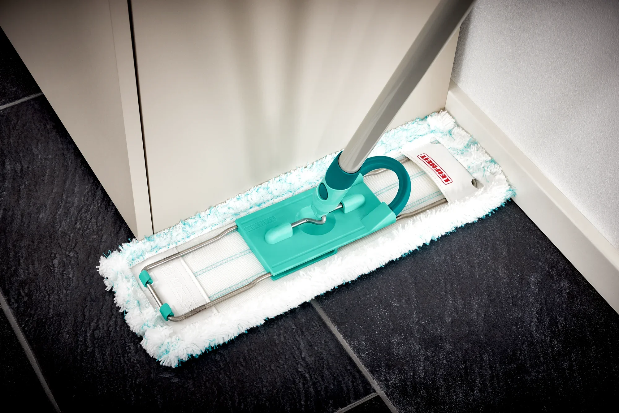 Un lavapavimenti Profi XL con manico in acciaio viene utilizzato in un angolo di una stanza. Il lavapavimenti ha un panno verde ed è ideale per una pulizia accurata.