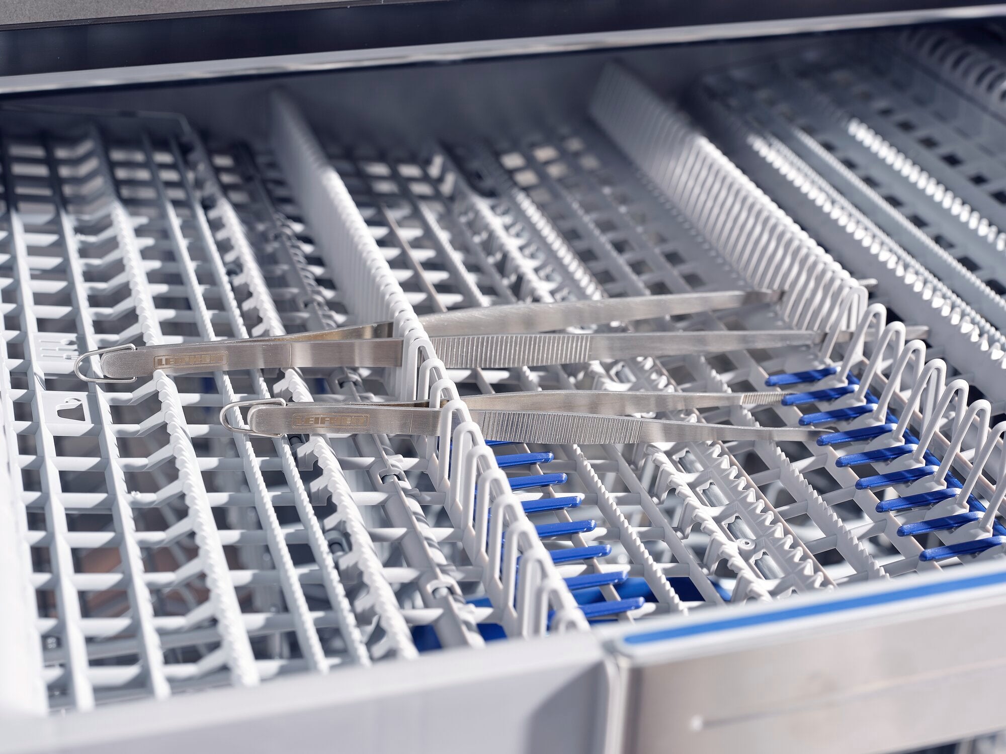 Deux pinces de cuisine de 30 cm sont posées sur une grille dans un lave-vaisselle. Les pinces sont en acier inoxydable et sont idéales pour saisir les aliments.