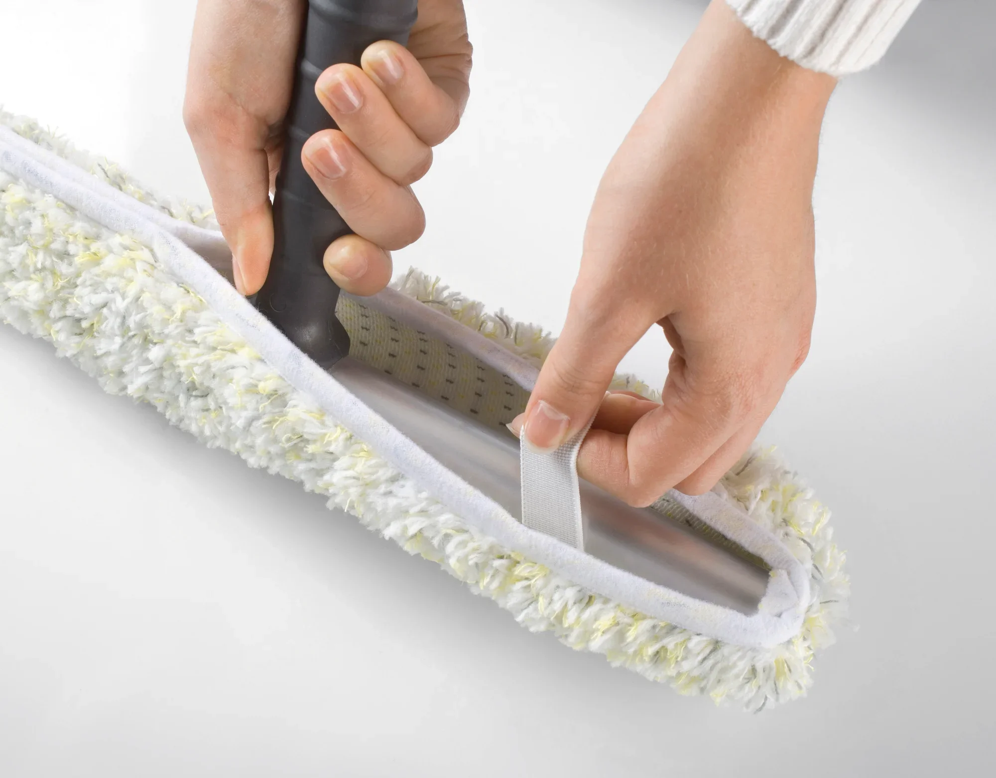 Eén paar handen bevestigt een Professional afdekzeil met enkele was van 45 cm aan een reinigingsapparaat. De overtrek heeft een donzig, wit oppervlak met gele accenten.