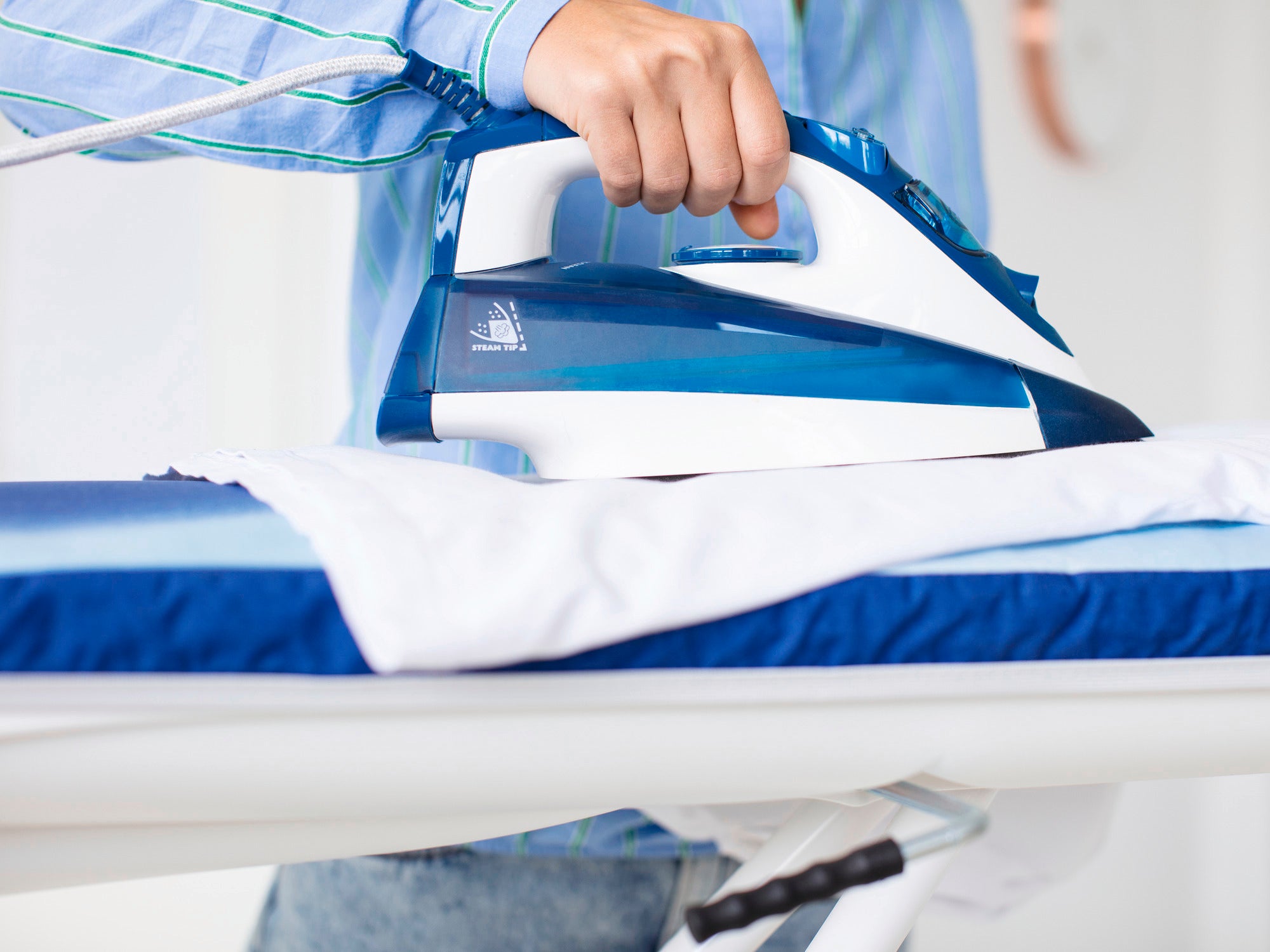 Bügelbrett Air Active M in Verwendung: Eine Person bügelt ein weißes Kleidungsstück auf einem blauen Bügelbrett mit einem modernen Dampfbügeleisen.