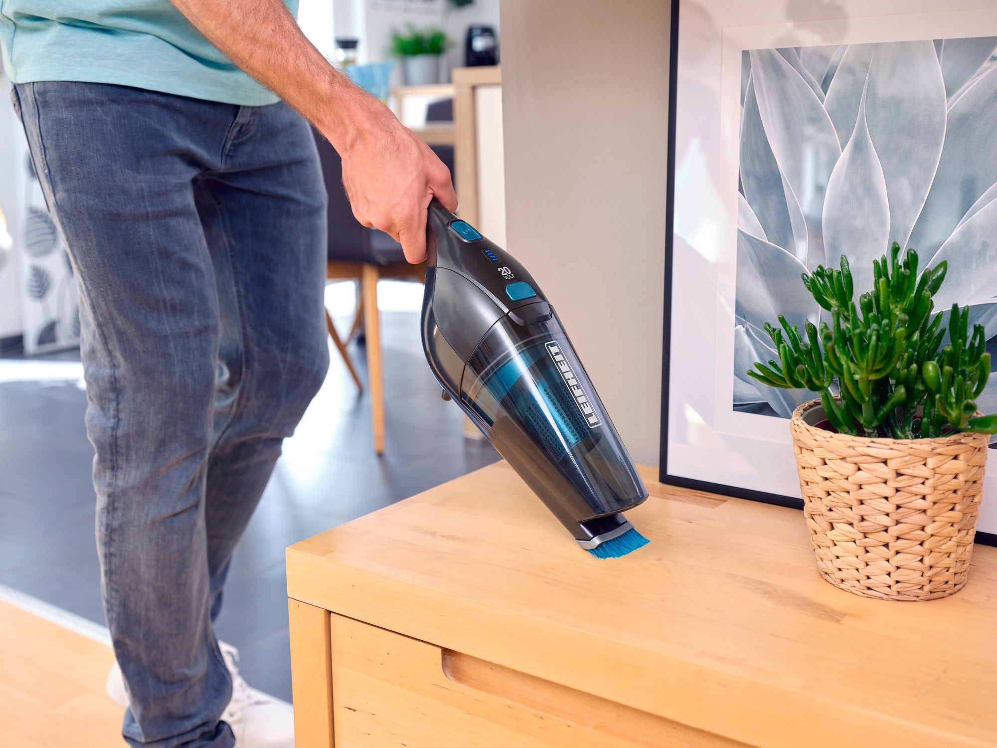Een man gebruikt de Rotaro PowerVac snoerloze stofzuiger om stof van een houten tafel te verwijderen. De stofzuiger is compact en snoerloos, ideaal om snel schoon te maken.