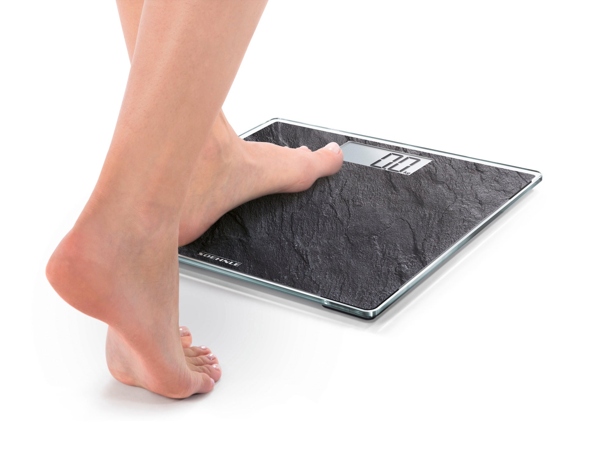 A person stands on the Style Sense Compact 300 Nature Edition digital bathroom scales in a slate finish. The scales have an elegant, natural surface and an easy-to-read display.