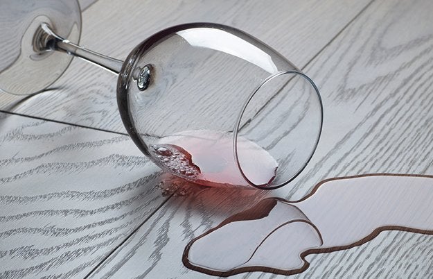Ein umgekipptes Weinglas auf hellem Holzboden, roter Wein ist herausgelaufen und bildet eine Pfuetze um das Glas herum.