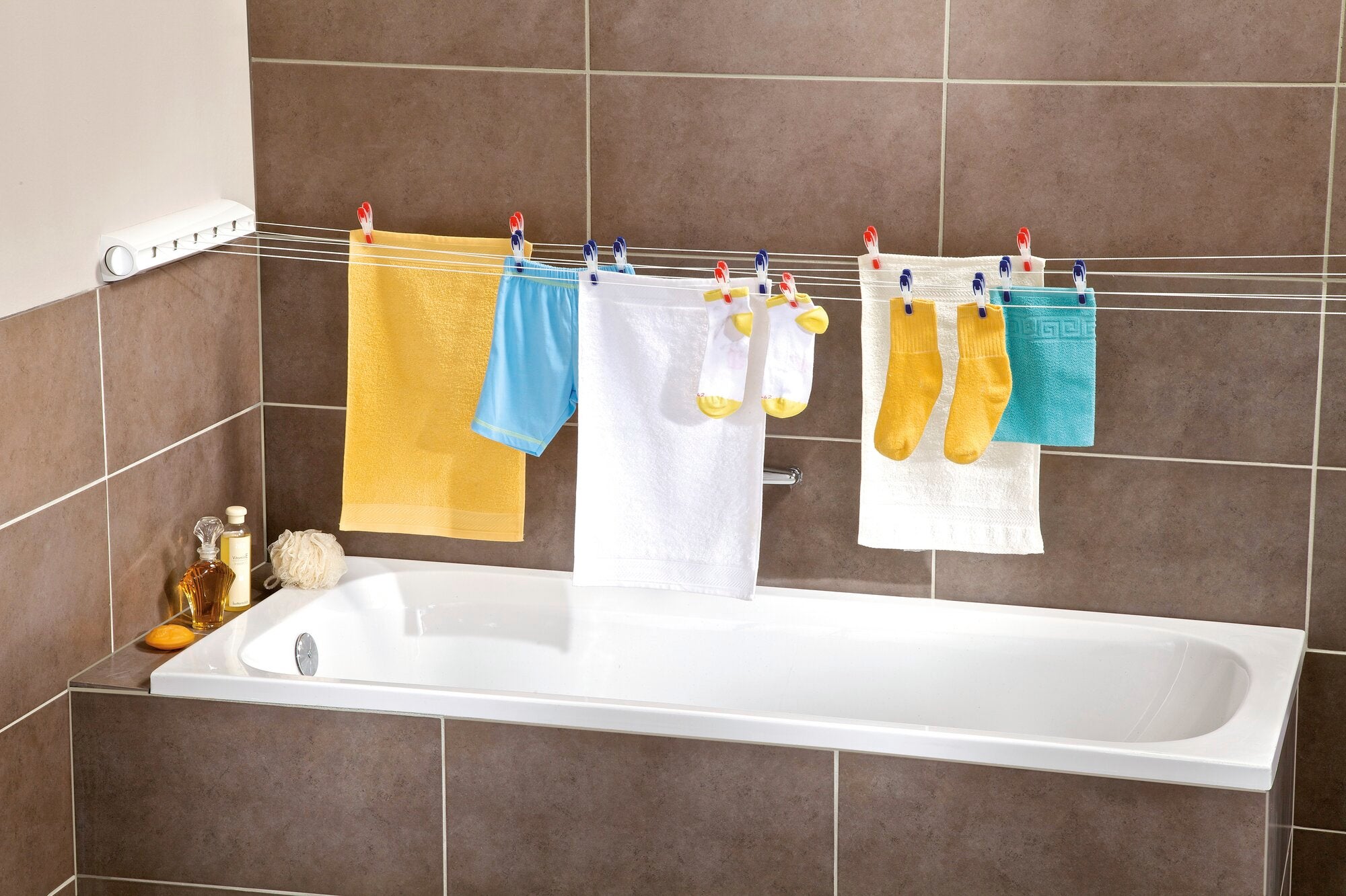 Wandtrockner Rollfix 210 Longline über einer Badewanne montiert, mit mehreren bunten Handtüchern und Socken, die zum Trocknen aufgehängt sind. Ideal für platzsparendes Trocknen.