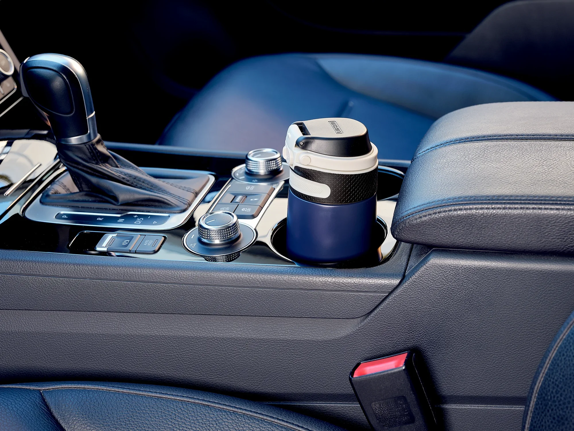 Izolowany kubek Flip 350 ml w kolorze ciemnoniebieskim, umieszczony w uchwycie samochodowym. Kubek ma praktyczną pokrywkę i idealnie pasuje do konsoli środkowej samochodu.