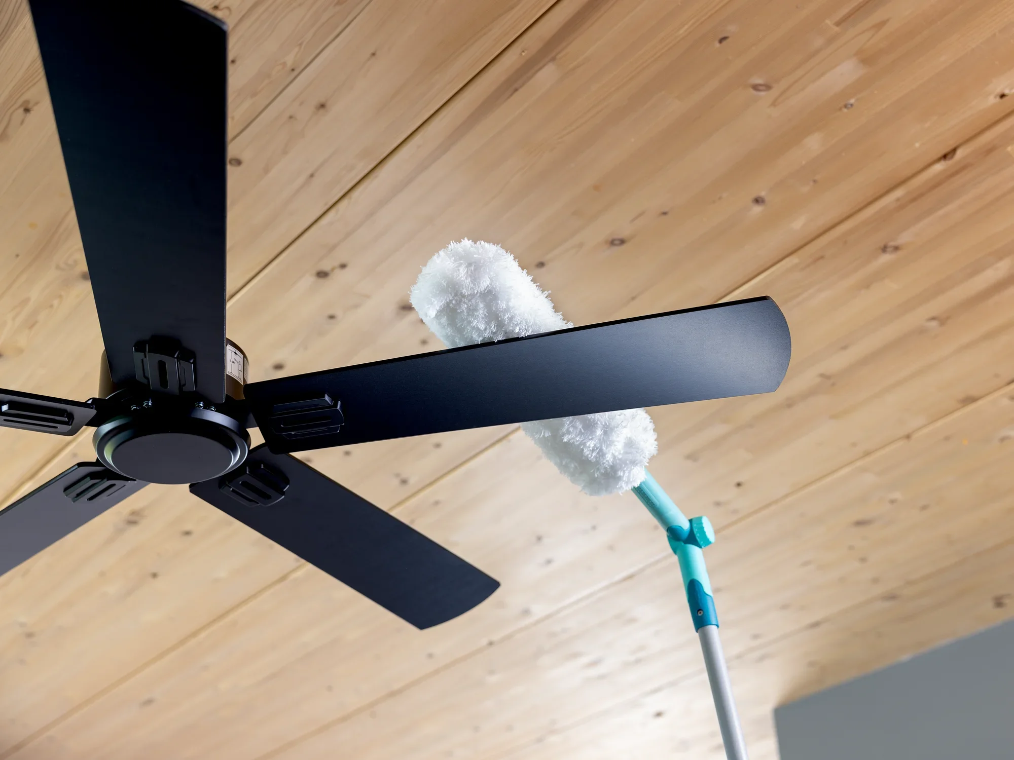 Een SUPERDUSTER XL Pro Reach plumeau reinigt de bladen van een plafondventilator. De plumeau heeft een lange steel, ideaal voor moeilijk bereikbare plaatsen.