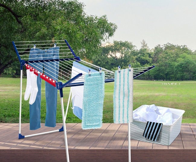 Ein Waeschestaender auf einer Terrasse mit Socken, Hosen und Handtuechern; daneben ein Waeschekorb, im Hintergrund eine Wiese.