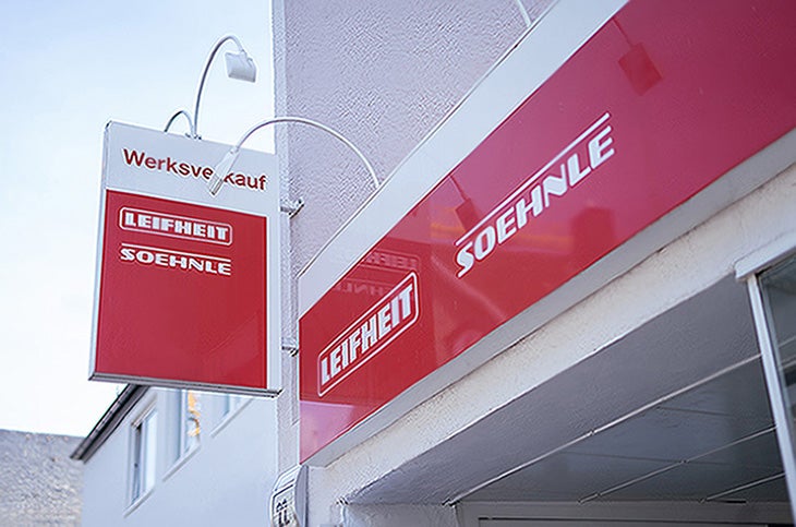 Rotes Ladenschild eines Werksverkaufs mit den weissen Logos der Marken Leifheit und Soehnle an einer Gebaeudefassade.