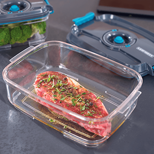 Frisches rotes Fleisch mit Kraeutern in einer transparenten Frischhaltebox, umgeben von weiteren Boxen, eine mit Brokkoli gefuellt.