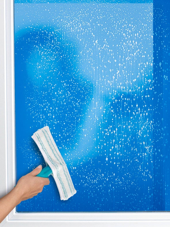 Ein Einwascher wird verwendet, um ein Fenster gründlich zu reinigen. Die Hand hält den Einwascher, während er über die nasse Glasoberfläche gleitet, um Schmutz zu entfernen.