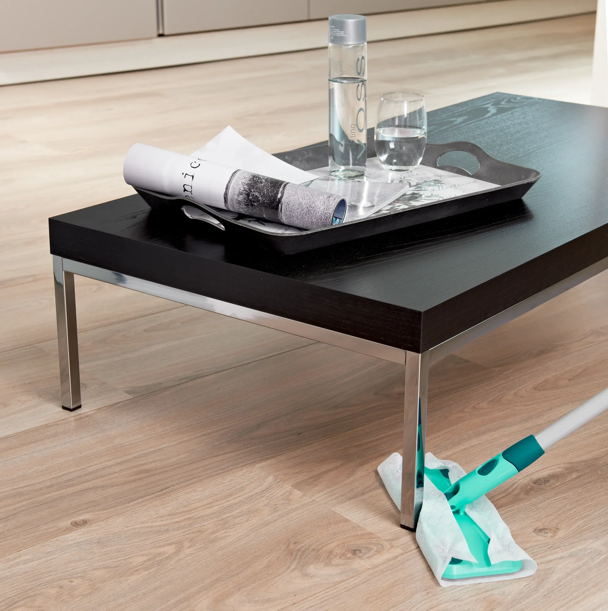 Una moderna mesa de salón con una bandeja que contiene una botella de agua y un vaso. Debajo se limpia el suelo con el set Clean and Away. Ideal para un entorno limpio.