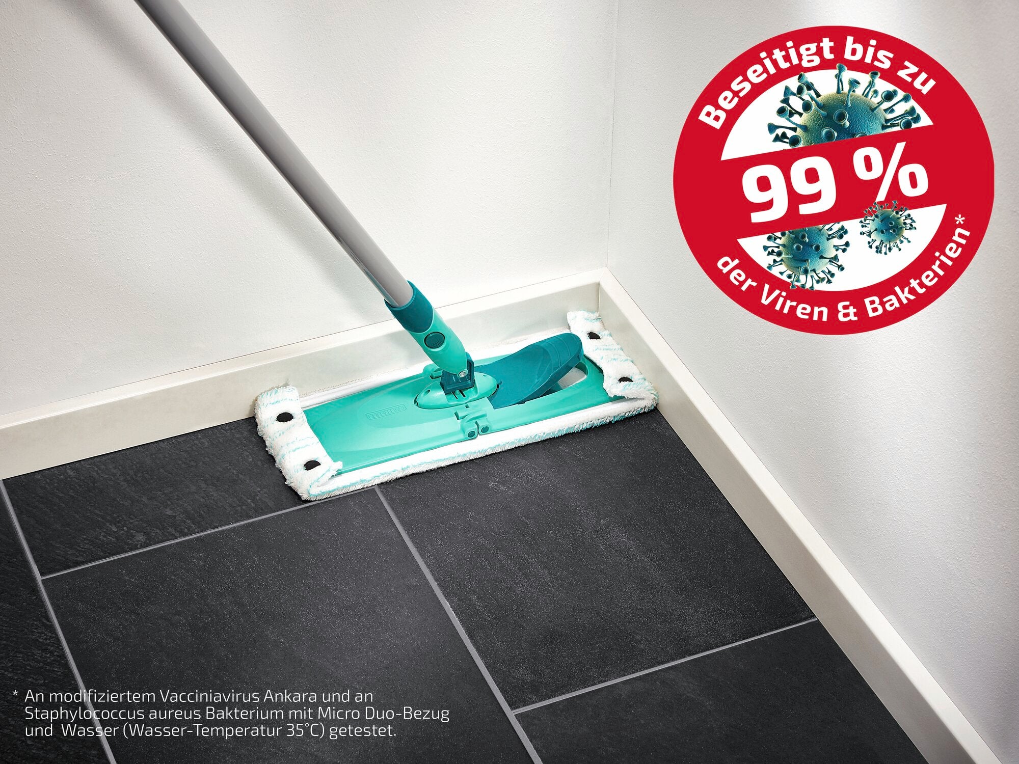 Ein Bodenwischer mit einem grünen Wischkopf reinigt eine schwarze Fliesecke. Ein rotes Siegel zeigt an, dass 99 % der Viren und Bakterien beseitigt werden. Ideal für hygienische Sauberkeit.