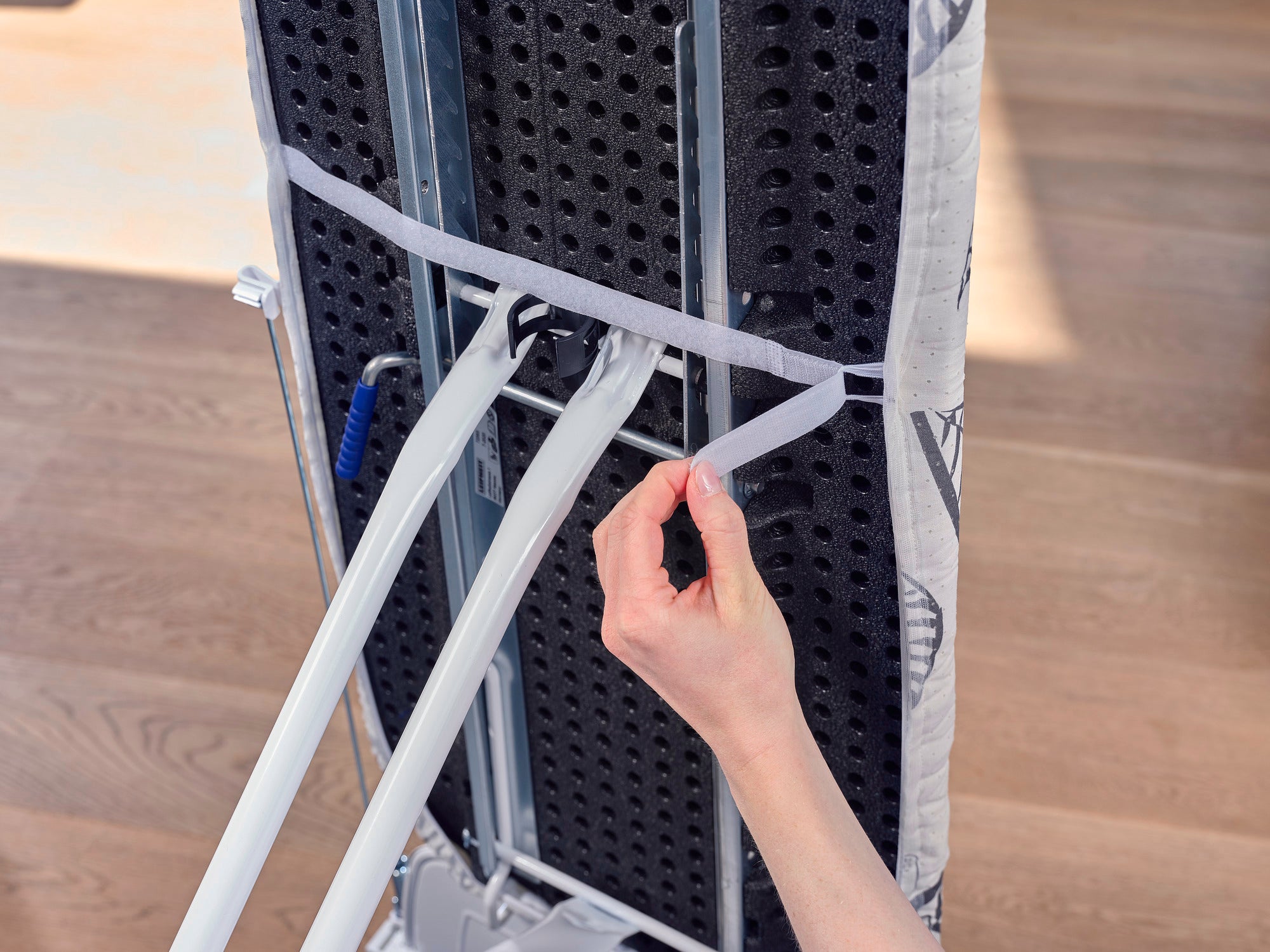 Ein Bügeltischbezug des Modells "Perfect Steam Air Board Express M" wird von einer Hand befestigt. Der Bezug ist mit einem elastischen Band gesichert, das für einen festen Sitz sorgt.