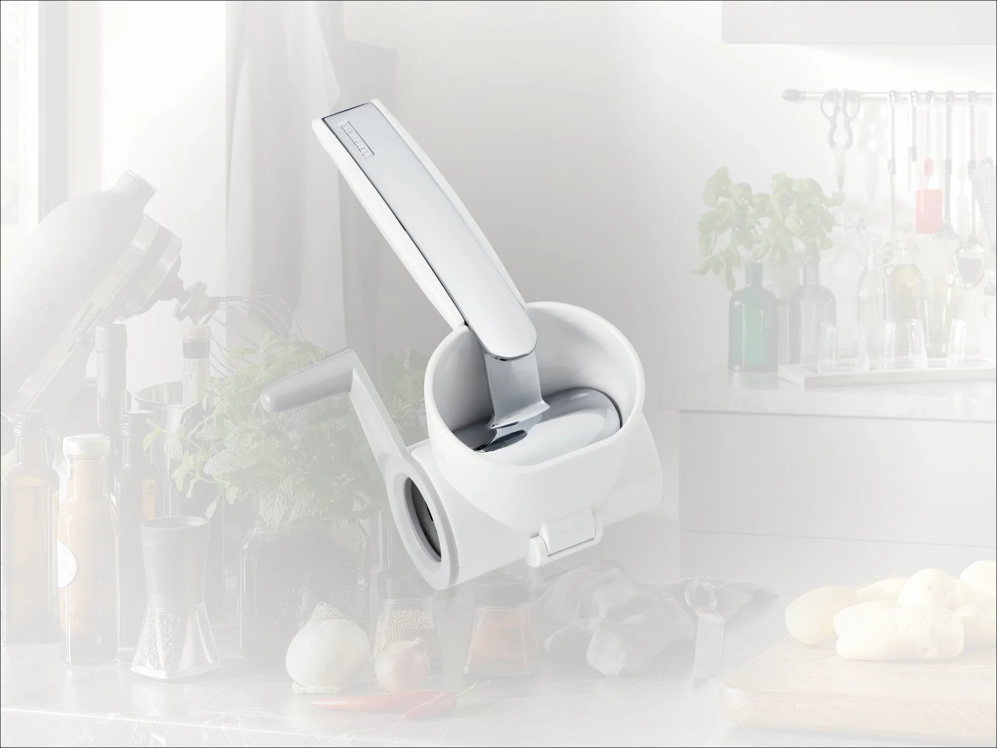 Un coupe-légumes argenté avec une poignée ergonomique est posé sur un plan de travail. Des ustensiles de cuisine et des herbes fraîches sont visibles à l'arrière-plan. Idéal pour hacher efficacement.