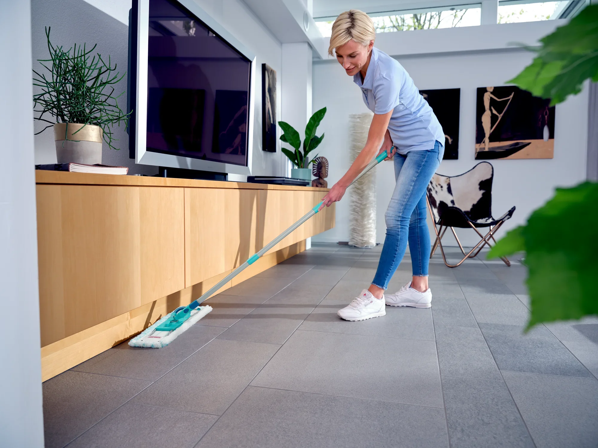 Een vrouw reinigt de vloer van een moderne woonkamer met de Profi XL vloerwisser. Het apparaat maakt een efficiënte reiniging mogelijk zonder te hoeven bukken. Ideaal voor grote oppervlakken.