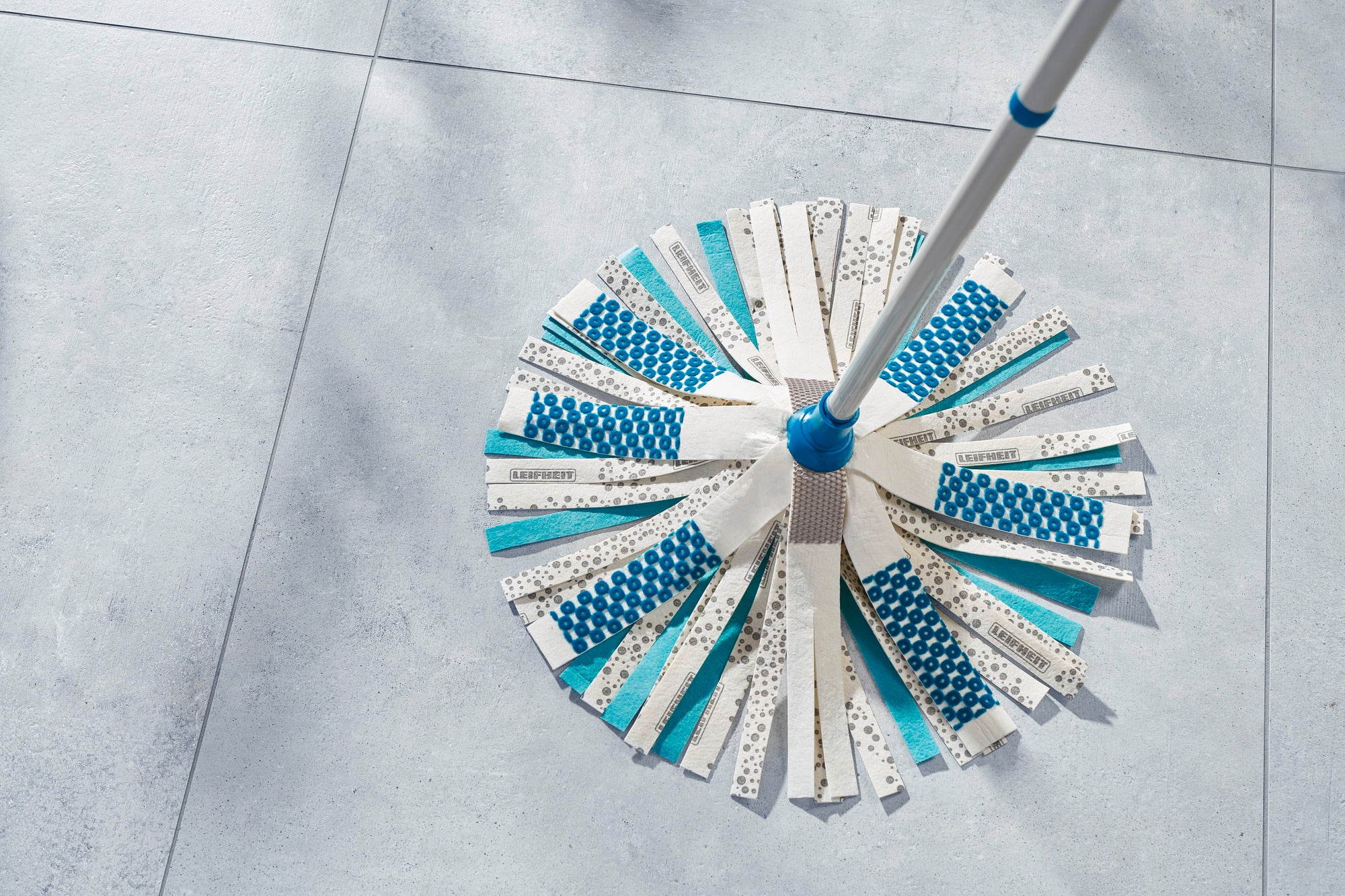 Un Power Mop 3in1 à rayures bleues et blanches repose sur un sol carrelé clair. La serpillière est photographiée sous un angle qui met en valeur la structure et le design des rayures.