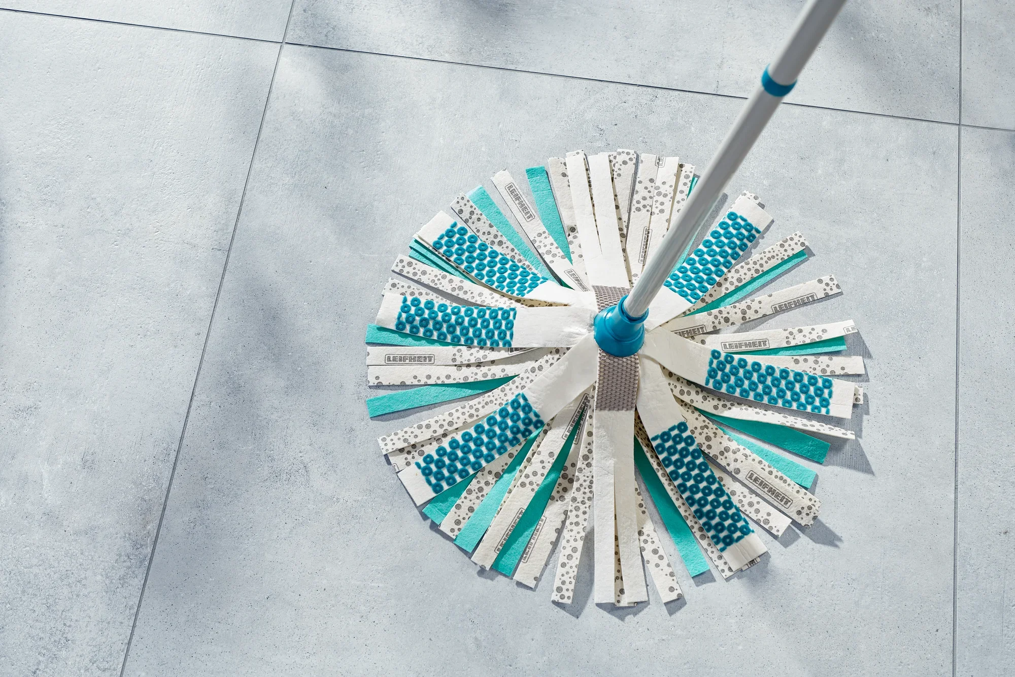 Ein Power Mop 3in1 mit blau-weißen Streifen liegt auf einem hellen Fliesenboden. Der Mop ist in einem Winkel fotografiert, der die Struktur und das Design der Streifen betont.