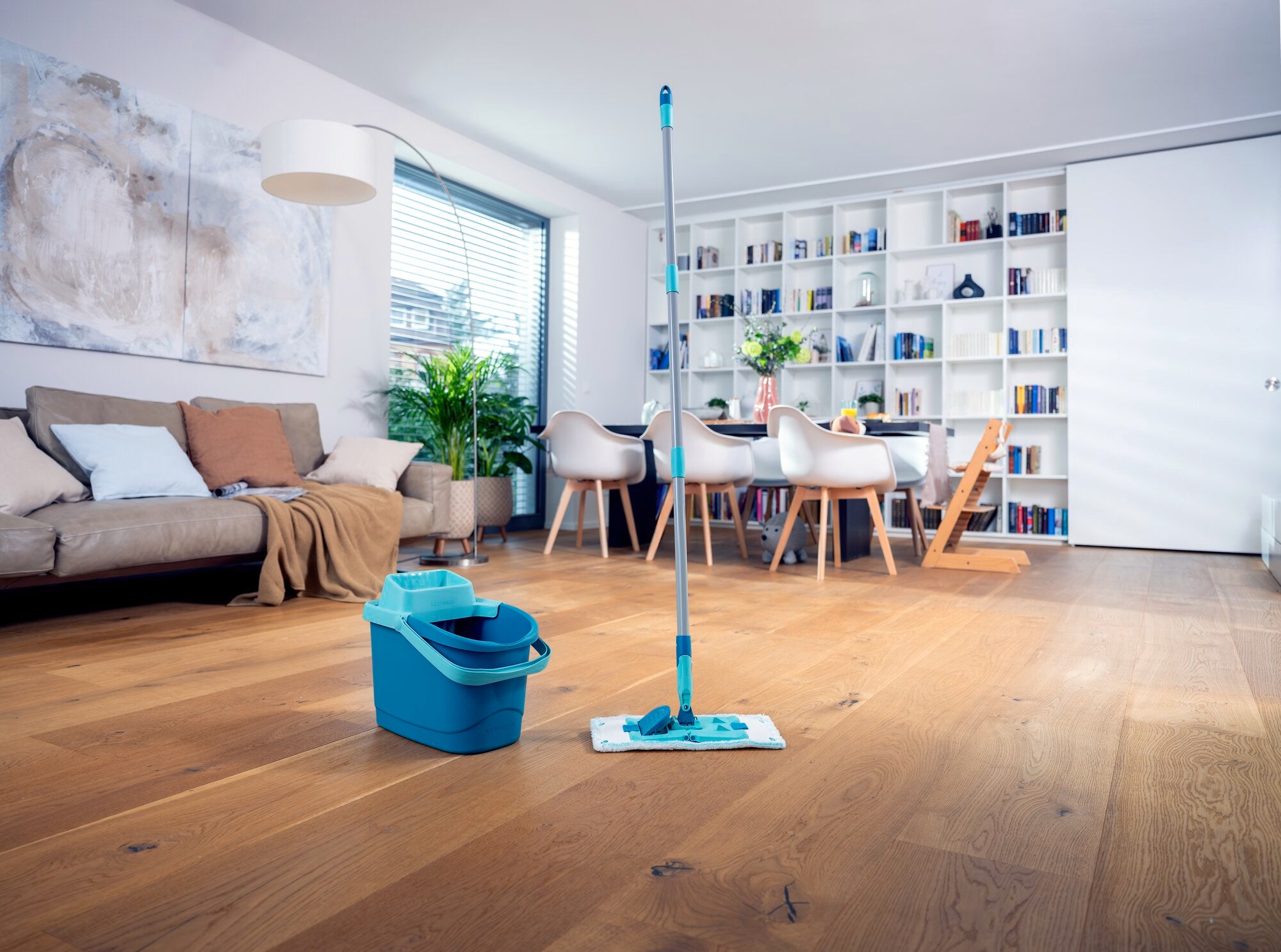 Ein stilvoll eingerichtetes Wohnzimmer mit einem modernen Holzboden. Im Vordergrund steht das POWER CLEAN Set, bestehend aus einem blauen Eimer und einem Wischmopp, bereit zur Reinigung.