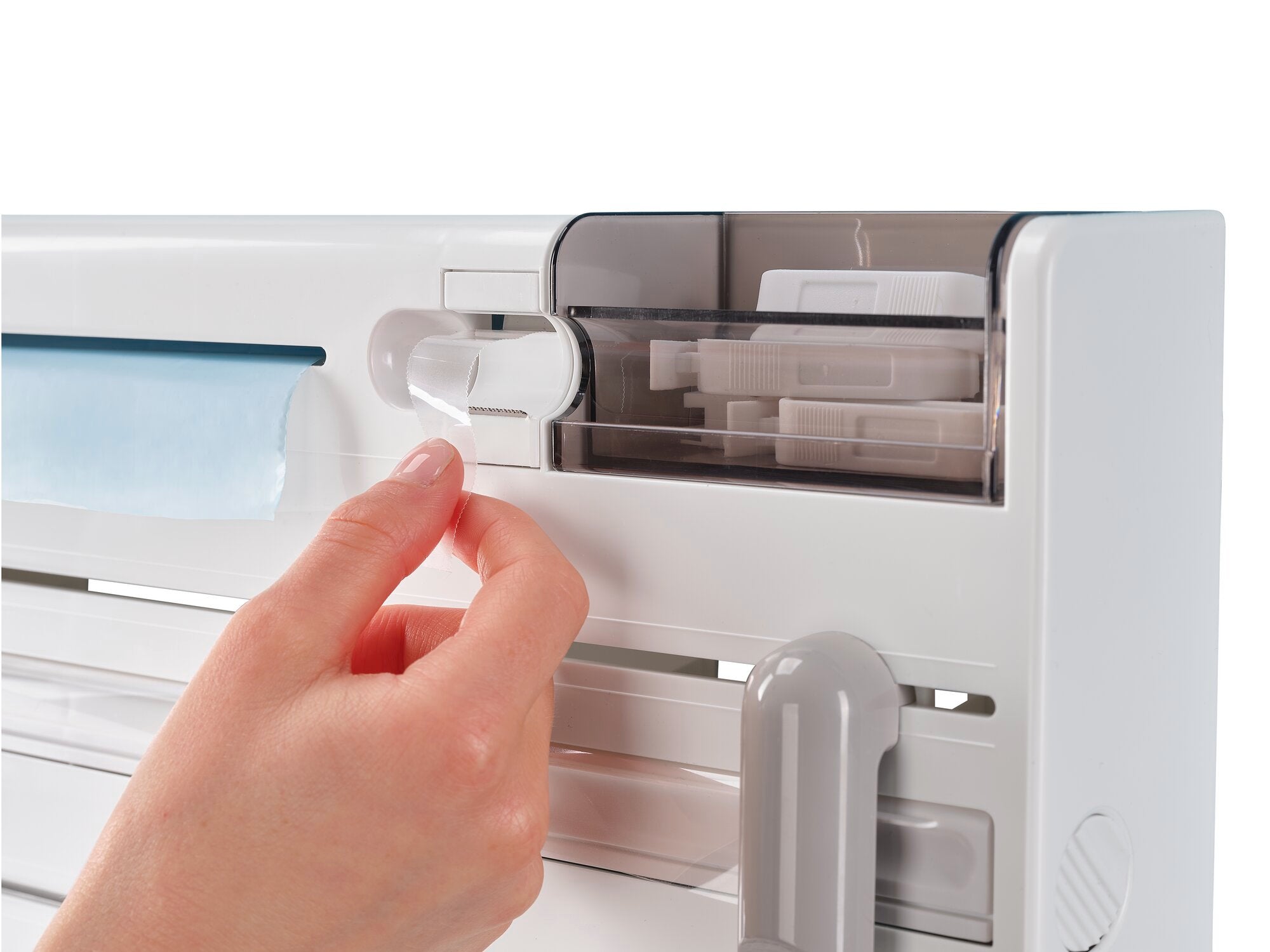 Ein Wandrollenhalter Parat Plus wird gezeigt. Eine Hand zieht an einem Hebel, um die Rolle zu wechseln. Der Halter ist weiß und hat ein transparentes Fach.