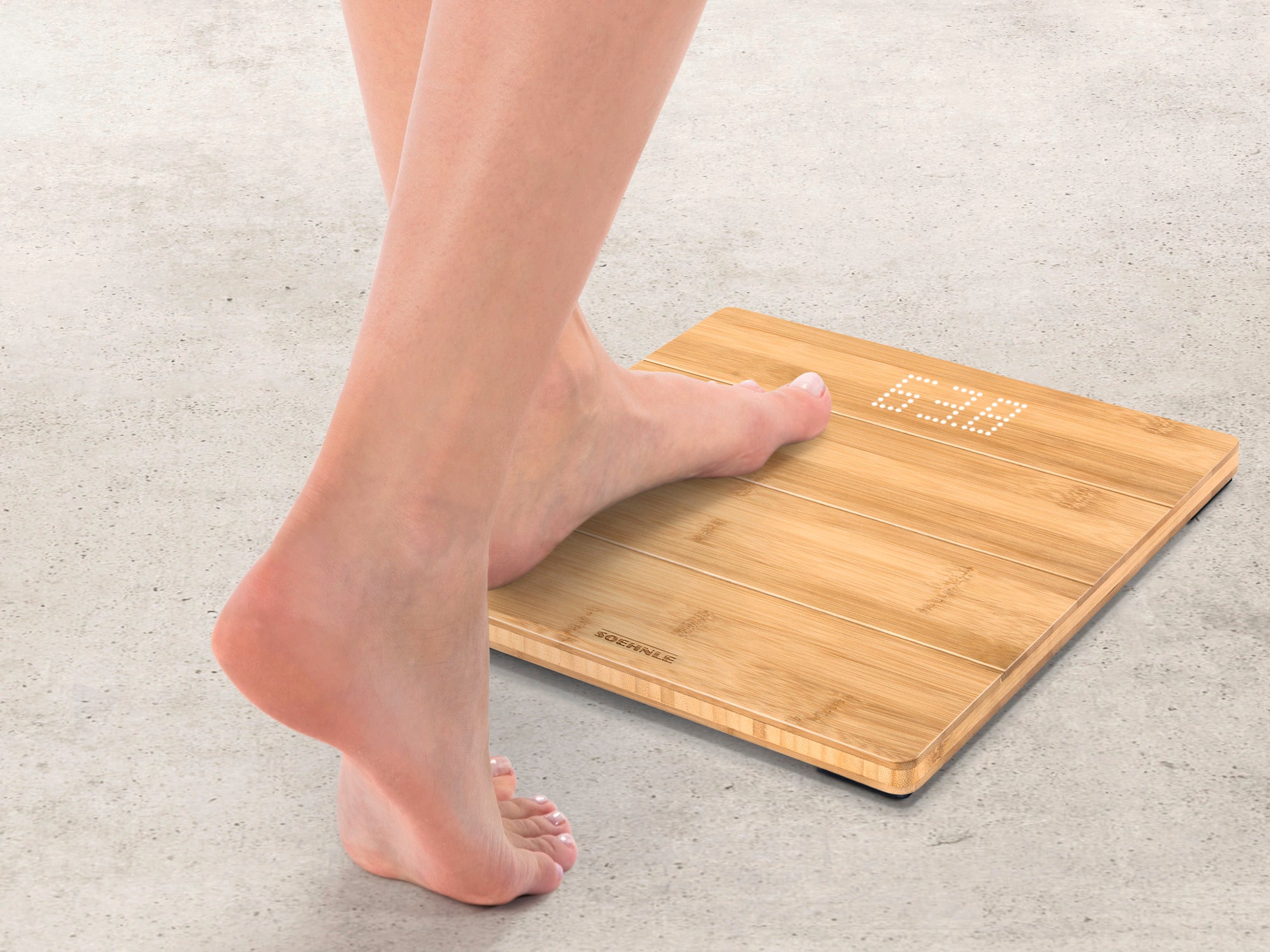 A person stands on the Style Sense Bamboo Magic digital bathroom scale. The scale has an elegant bamboo surface and shows the weight on a digital display.