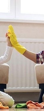Zwei Personen geben sich in einem Raum ein High-Five, tragen gelbe Gummihandschuhe, umgeben von bunten Reinigungstuechern.
