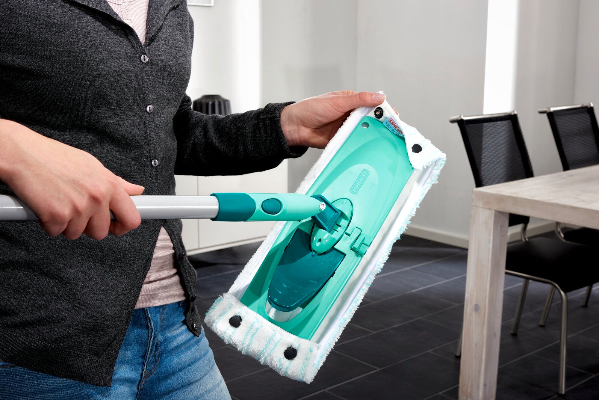A person is holding the Combi M floor mop, which is equipped with a green cleaning head. The mop is ideal for thorough cleaning of floors in modern living spaces.