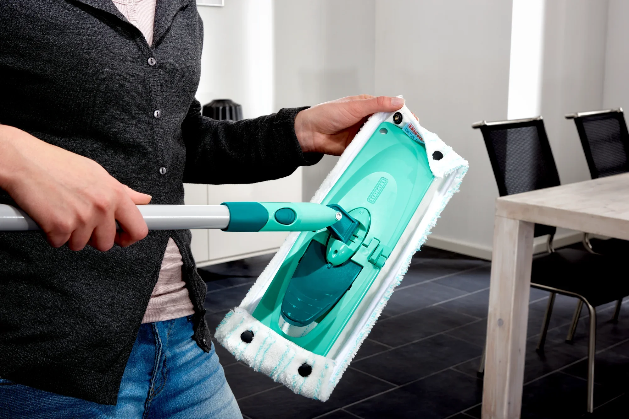 A person is holding the Combi M floor mop, which is equipped with a green cleaning head. The mop is ideal for thorough cleaning of floors in modern living spaces.