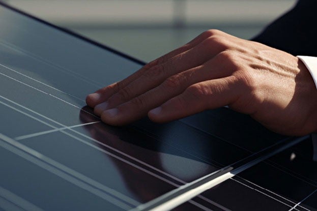 Eine Hand beruehrt eine glaenzende Solarzelle, die das Sonnenlicht reflektiert, mit sichtbaren Linien und einem leicht verschwommenen Hintergrund.