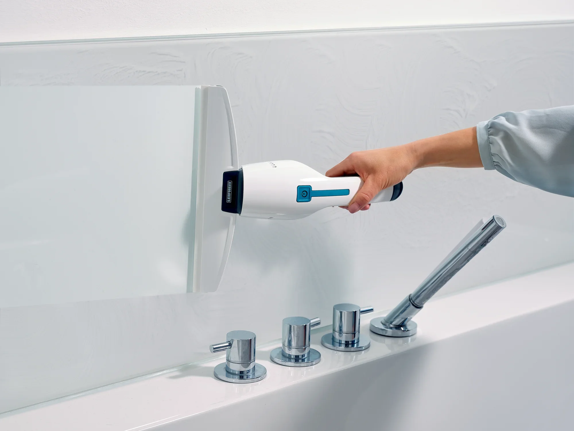 Jedna osoba używa odkurzacza do okien i wanien Nemo do czyszczenia gładkiej szklanej powierzchni. Odkurzacz jest biały z niebieskimi akcentami i jest używany w nowoczesnej łazience.