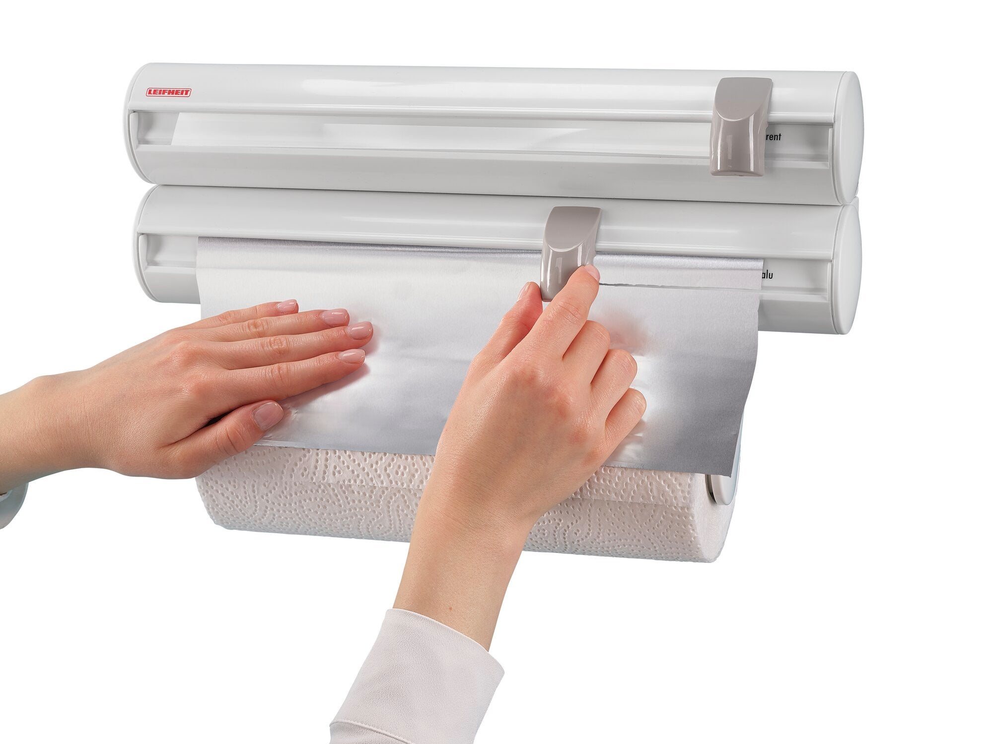 Un support mural Rolly Mobil est utilisé pour couper du papier aluminium. Deux mains actionnent le support fixé au mur. Idéal pour la cuisine et le ménage.