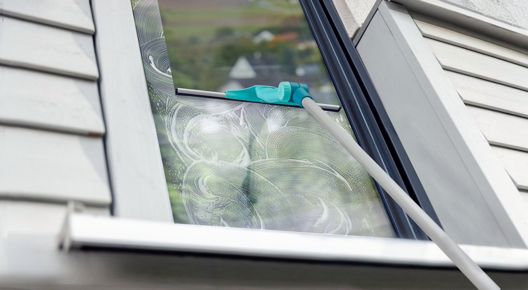 Ein Fensterreiniger mit Teleskopstange, der WindowSlider 2in1 XL ProReach, wird verwendet, um ein schräges Fenster zu reinigen. Der blaue Reinigungskopf gleitet über die Glasoberfläche.