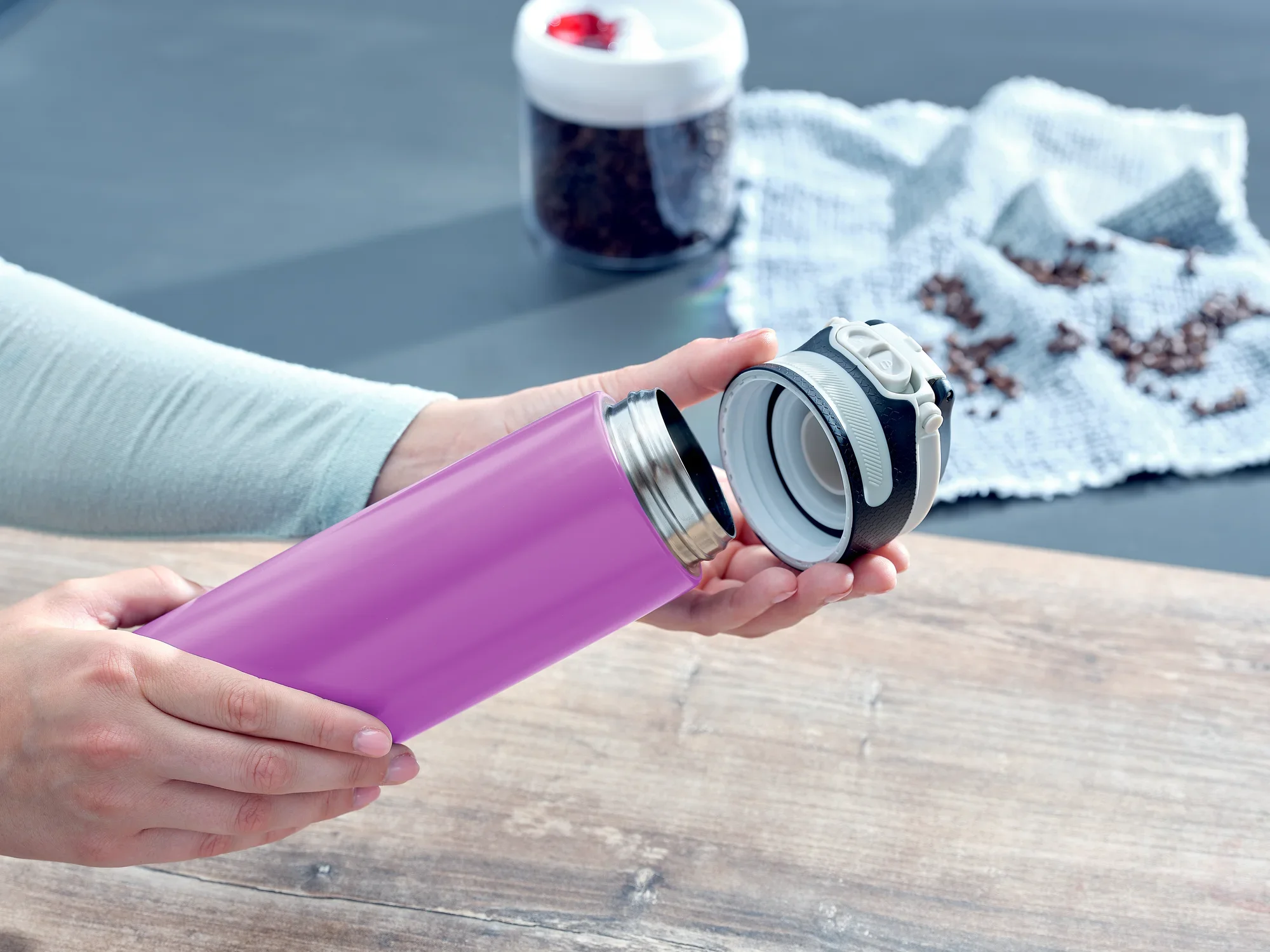 Flip 600 ml vacuümmok in paars wordt geopend. Op de achtergrond zijn koffiebonen en een doek te zien. De mok is ideaal voor onderweg en houdt drankjes warm of koud.