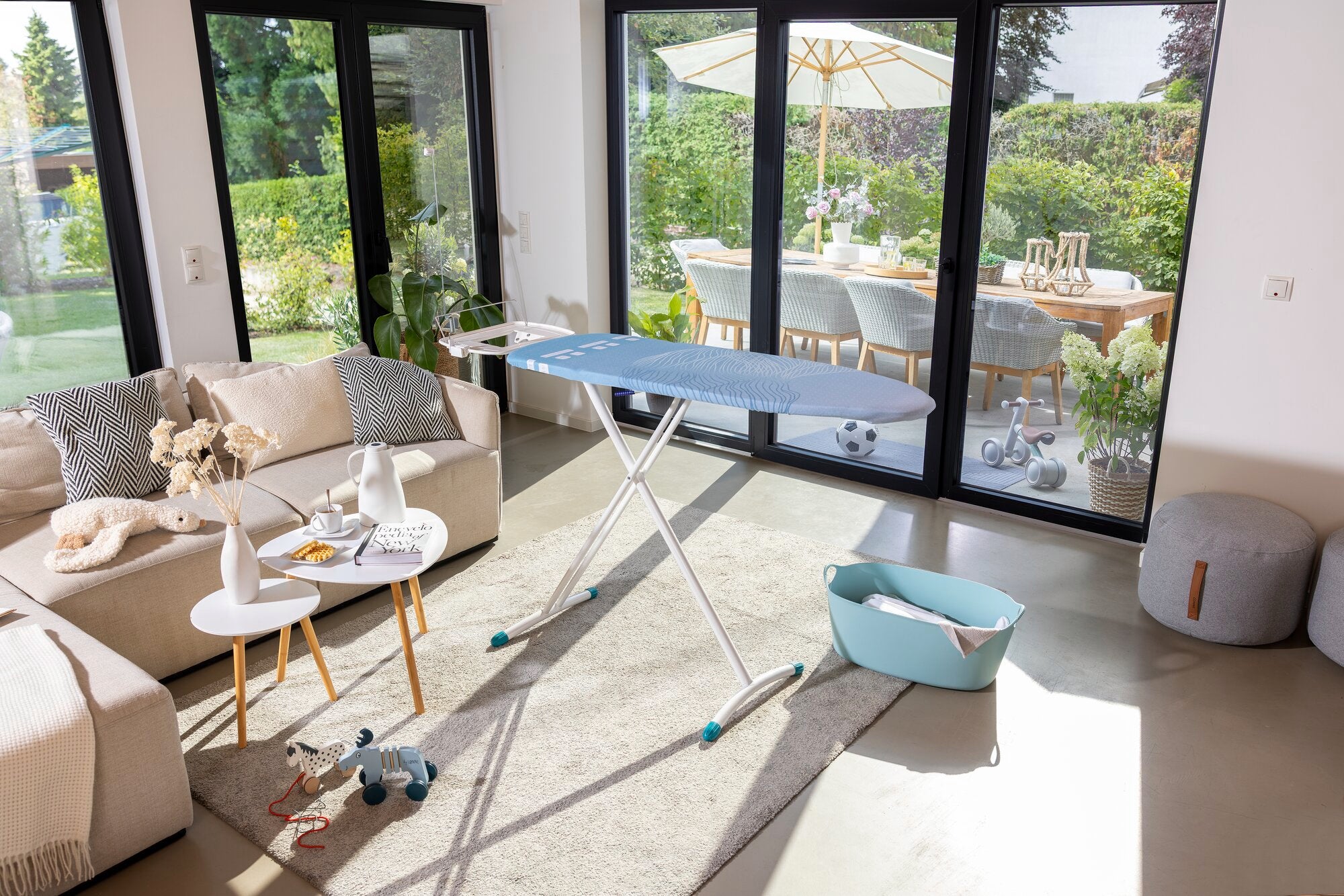 Bügelbrett Leifheit Air Board Express M Solid in einem modernen Wohnzimmer mit großen Fenstern. Das Brett steht auf einem Teppich, umgeben von stilvollen Möbeln und Dekorationen.
