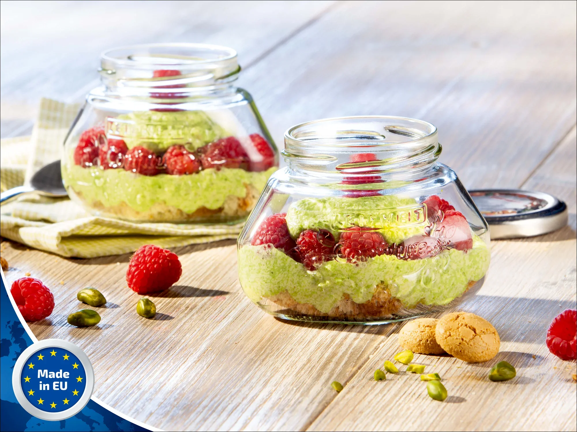 Zwei Leifheit Gelee-Gläser mit 1,4 Liter Fassungsvermögen stehen auf einem Holztisch. Sie sind mit grünem Dessert, Himbeeren und Keksen gefüllt. Ein "Made in EU"-Logo ist sichtbar.