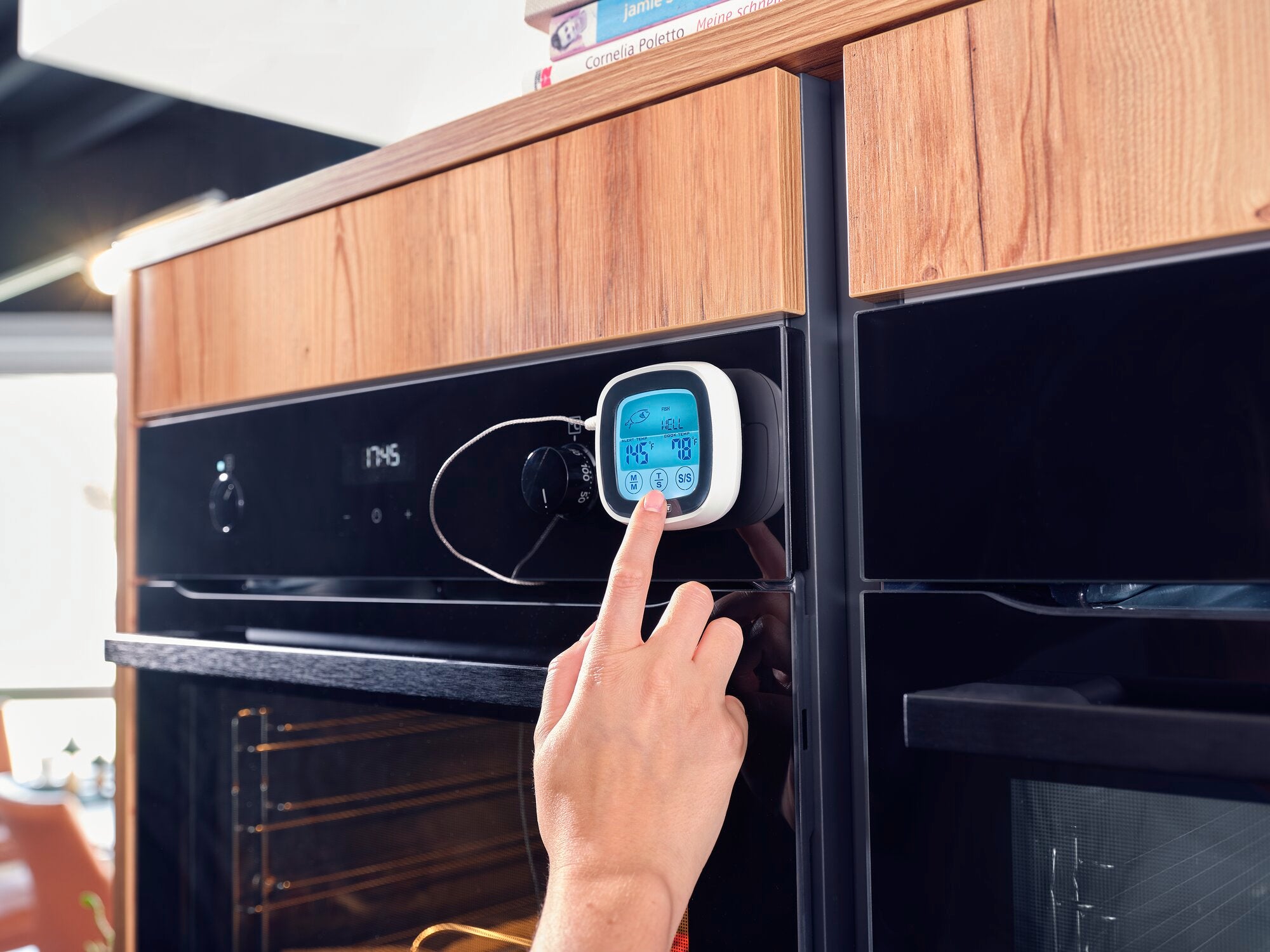 Ein Braten- und BBQ-Thermometer ist an einem modernen Backofen angebracht. Eine Hand bedient das digitale Display, das Temperaturinformationen anzeigt. Ideal für präzises Kochen.