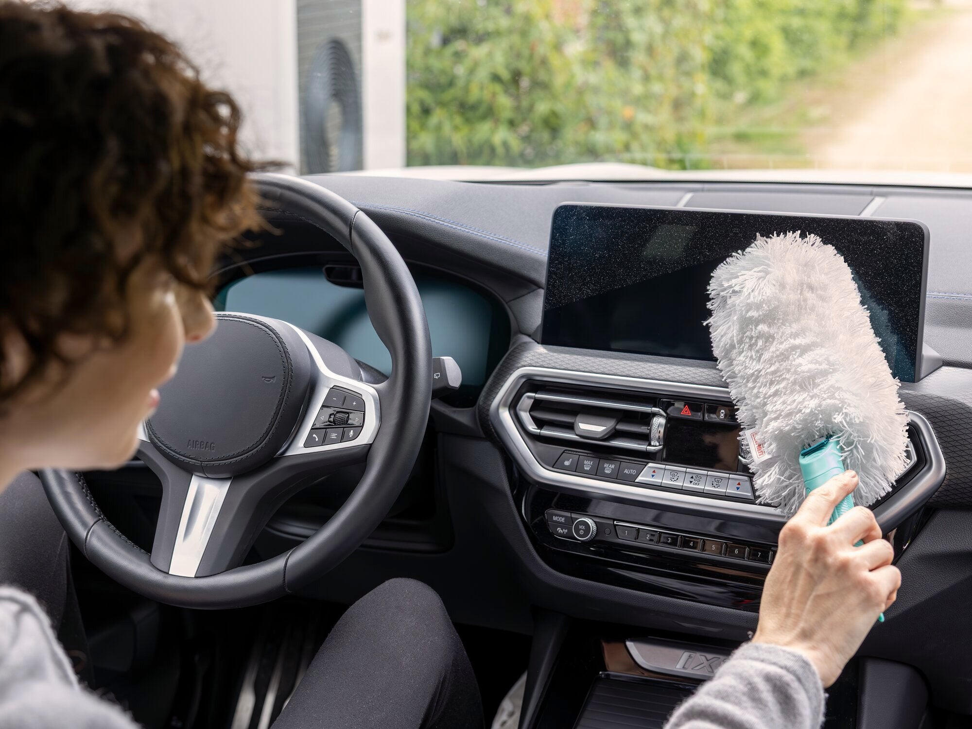 Une personne utilise le plumeau SUPERDUSTER pour nettoyer le tableau de bord d'une voiture. Le plumeau a des fibres blanches et est passé délicatement sur la surface.