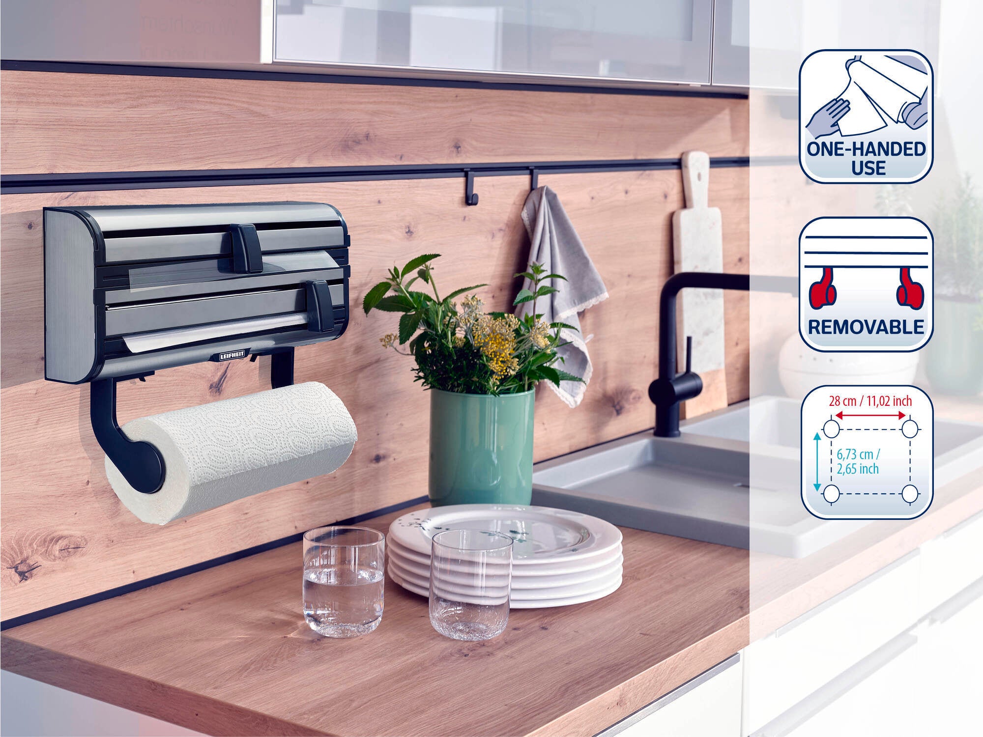 Wall-mounted Leifheit kitchen roll holder with integrated foil cutter, mounted in a modern kitchen. Includes symbols for one-handed operation, removable and dimensions. Ideal for efficient kitchen organisation.