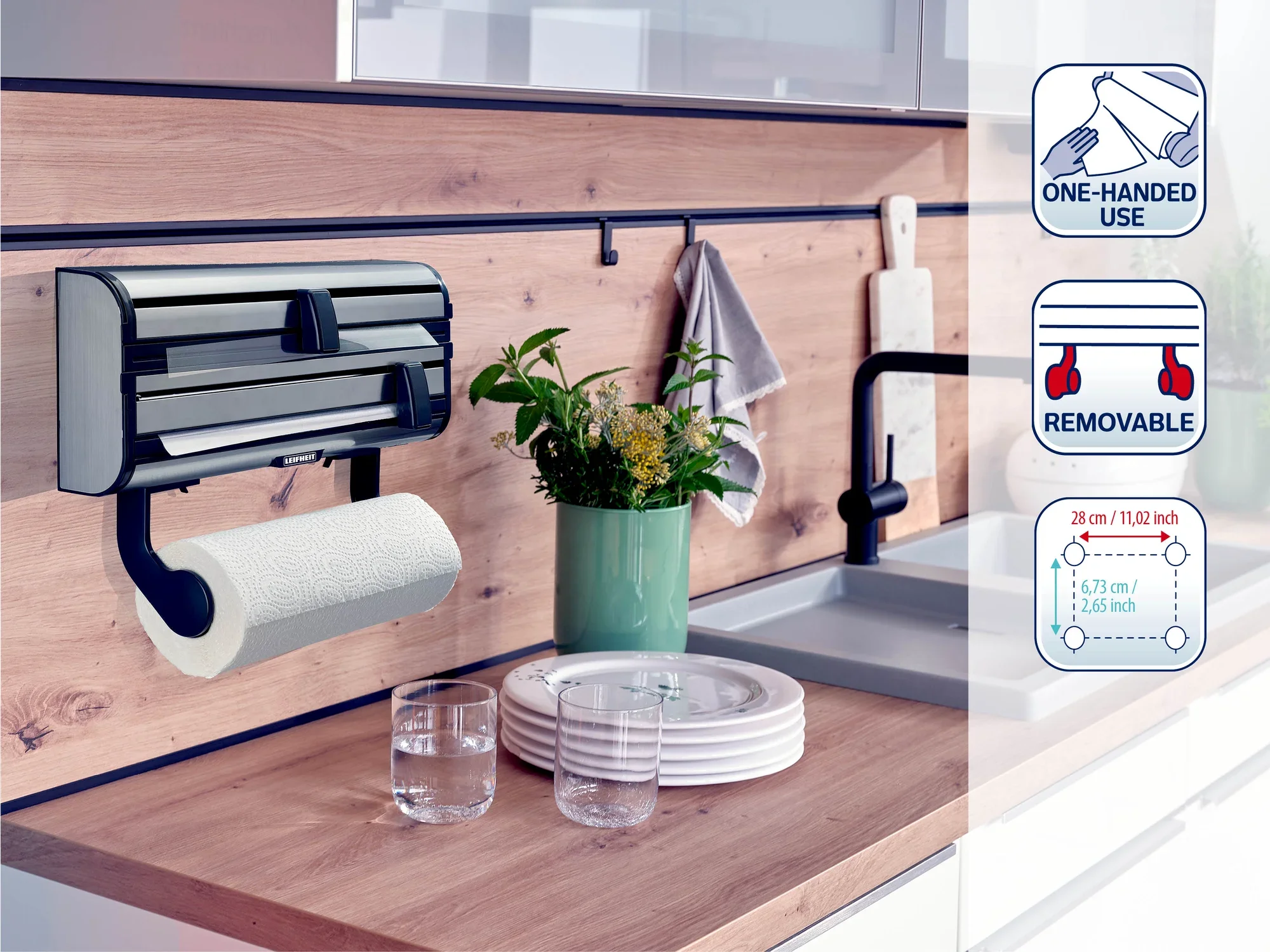 Naścienny uchwyt na rolki kuchenne Leifheit ze zintegrowanym obcinaczem do folii, montowany w nowoczesnej kuchni. Zawiera symbole obsługi jedną ręką, możliwość demontażu i wymiary. Idealny do efektywnej organizacji kuchni.