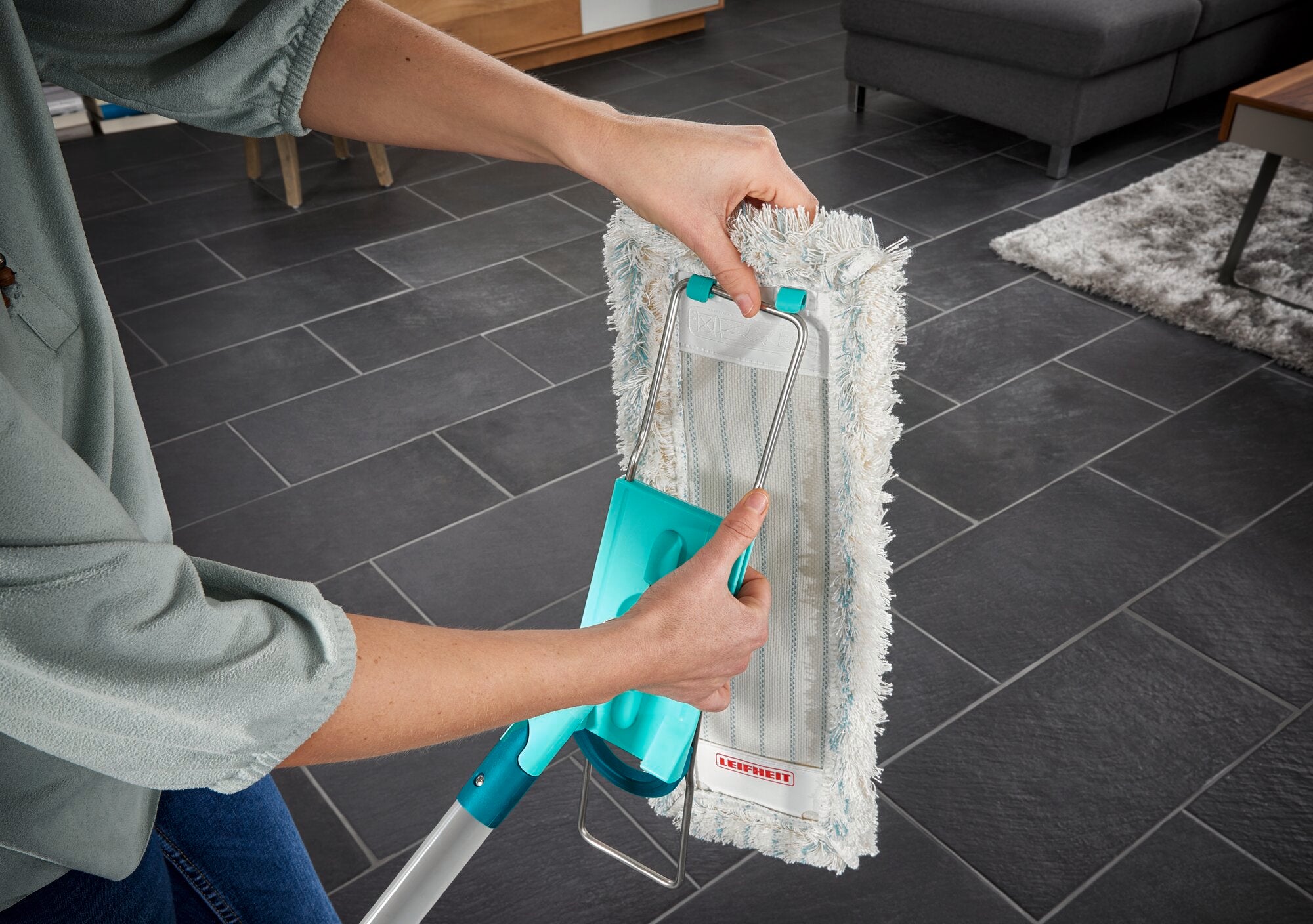 Une personne utilise la serpillière Profi XL pour nettoyer un sol carrelé foncé. La serpillière est dotée d'une housse en coton et d'une poignée stable pour un nettoyage efficace.